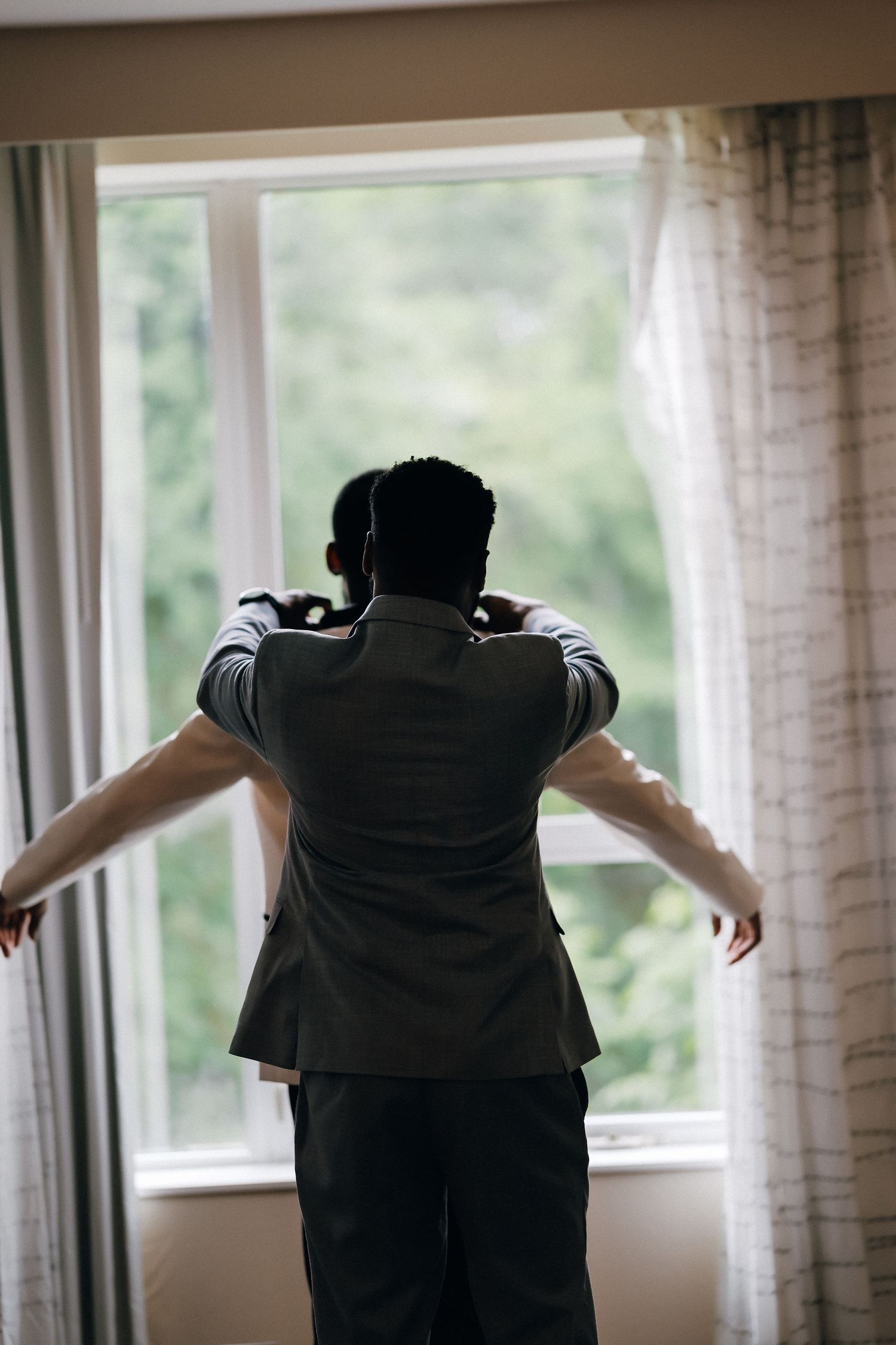 Groom standing at window opening curtains before wedding ceremony.