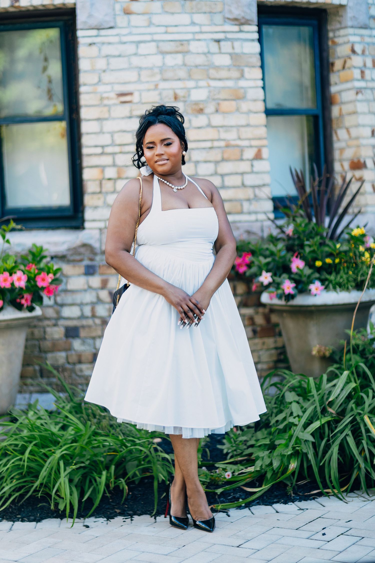 Black bride in a vintage-style white halter tea-length dress posing before a stone building.