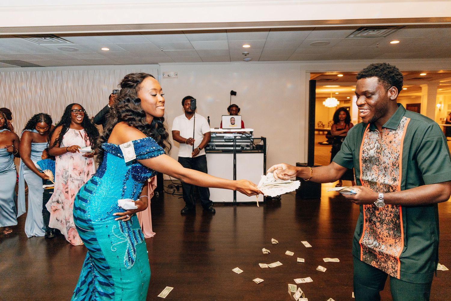 Guests spraying money on bride in blue African dress at wedding reception.