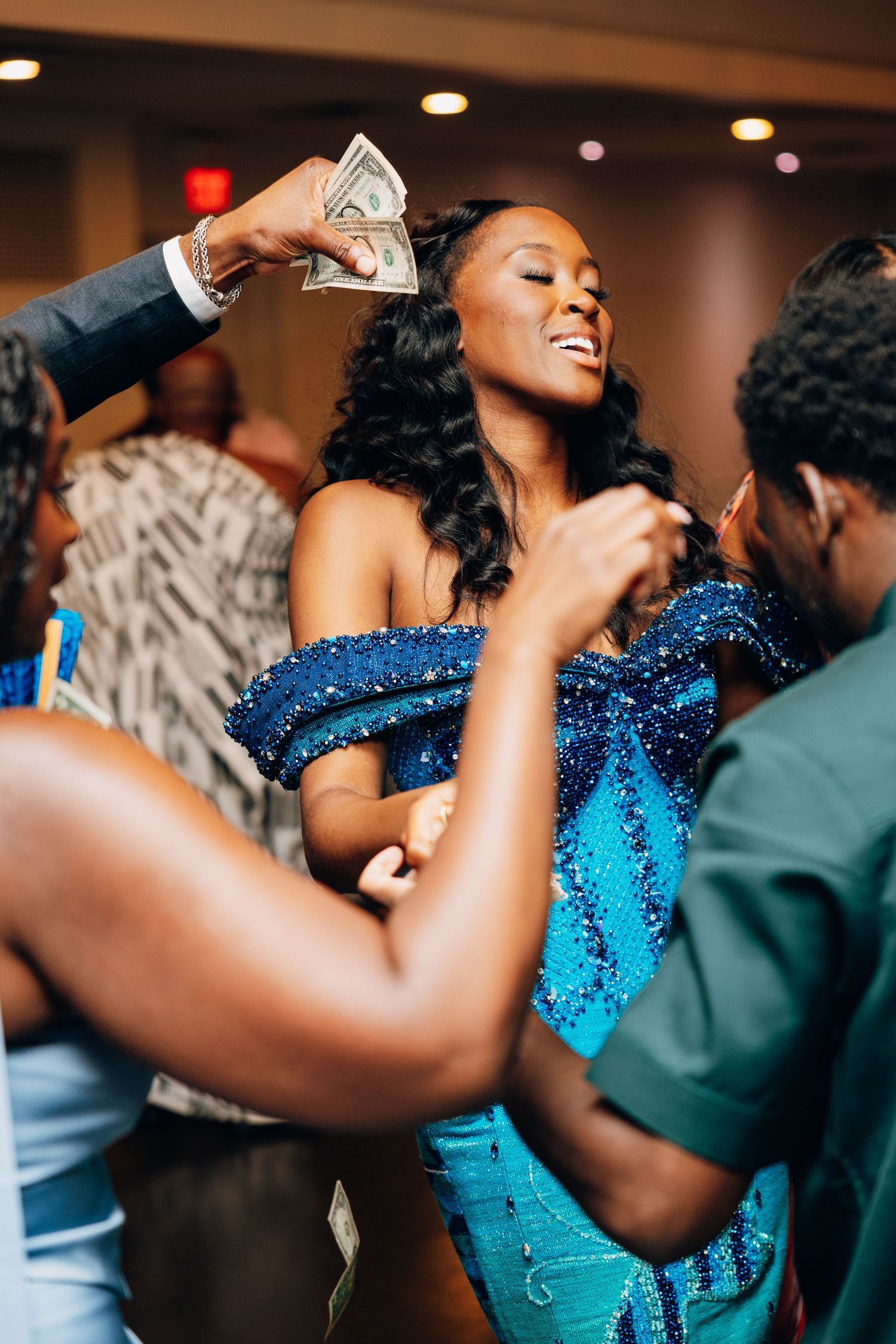 Bride in blue sequin gown being sprayed with money at African wedding reception.