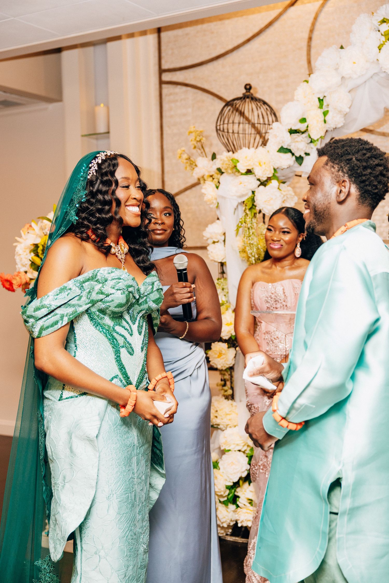 Bride in teal gown laughs with groom in mint suit during wedding ceremony with bridal party.