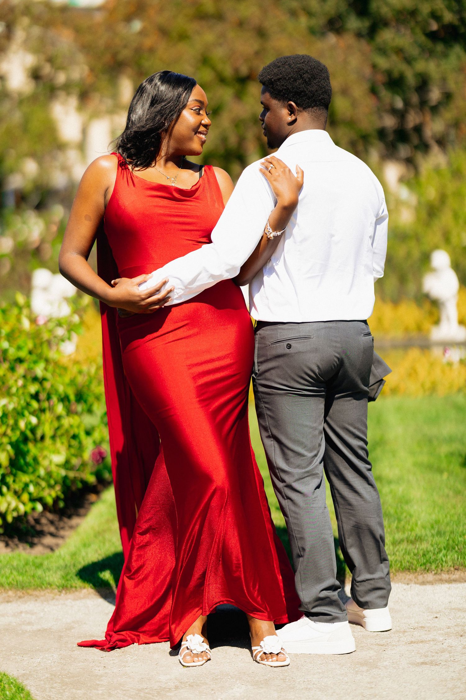 Couple gazing at each other in bright garden, woman in red dress and man in white shirt.