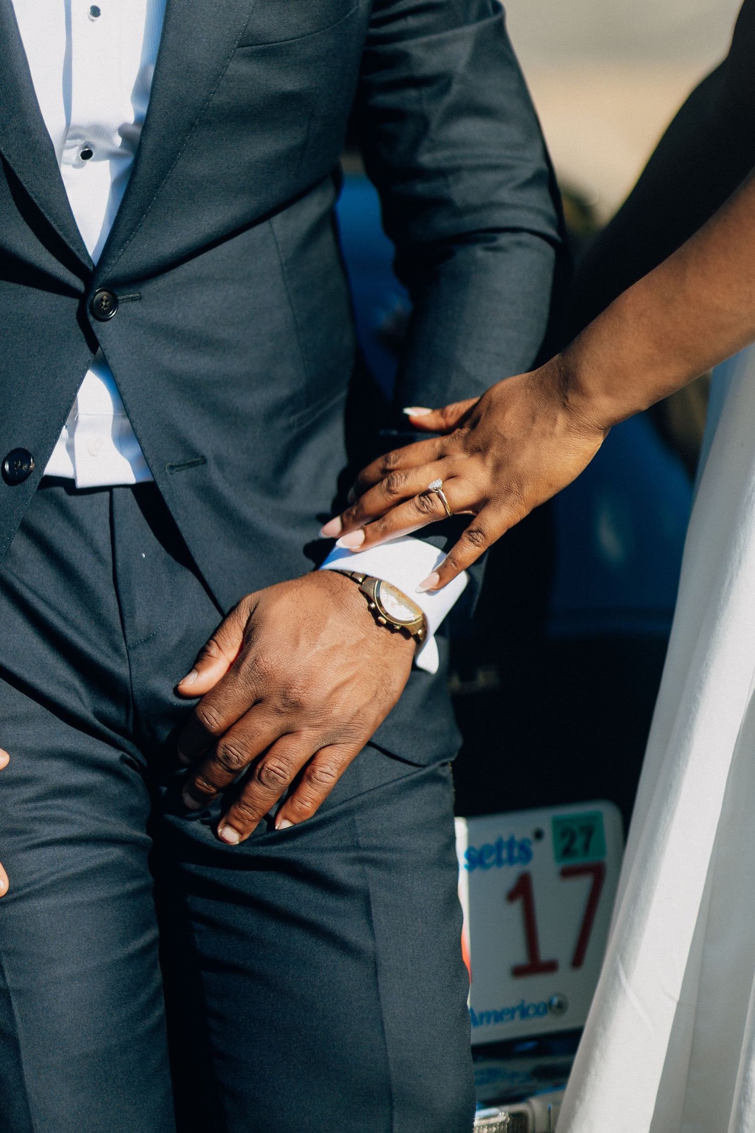 Close-up of bride and groom holding hands, showcasing wedding rings and groom's gold watch.