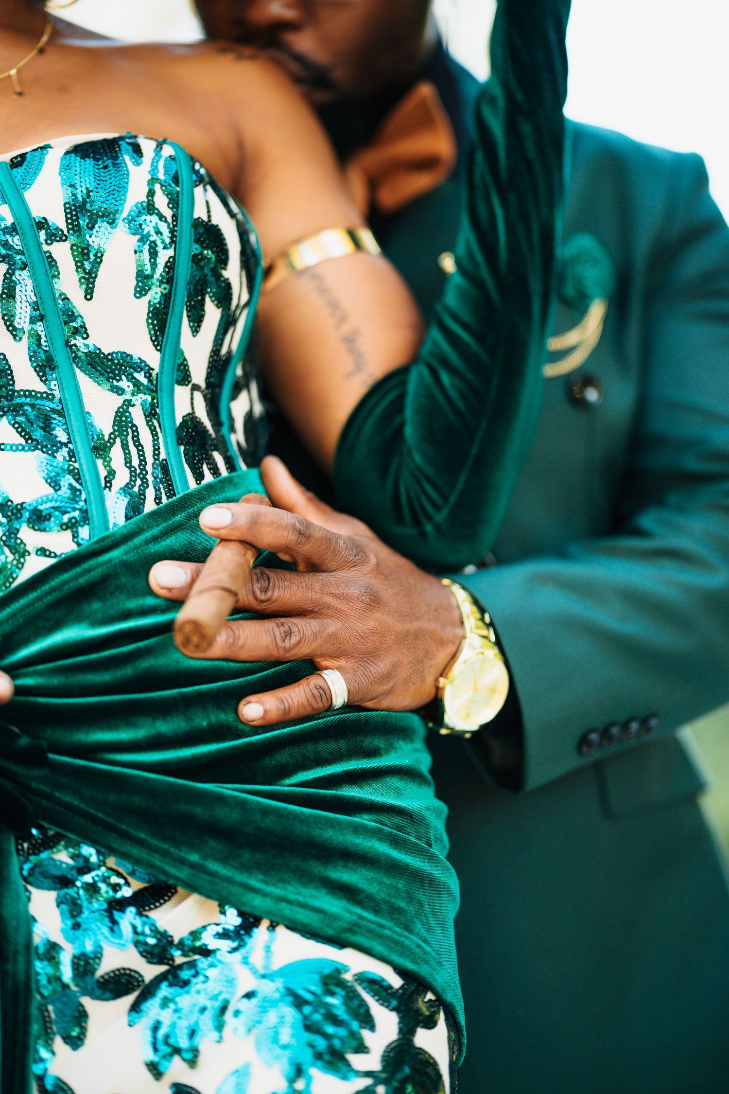 Close-up of couple embracing, showing green velvet sash and gold watch details.