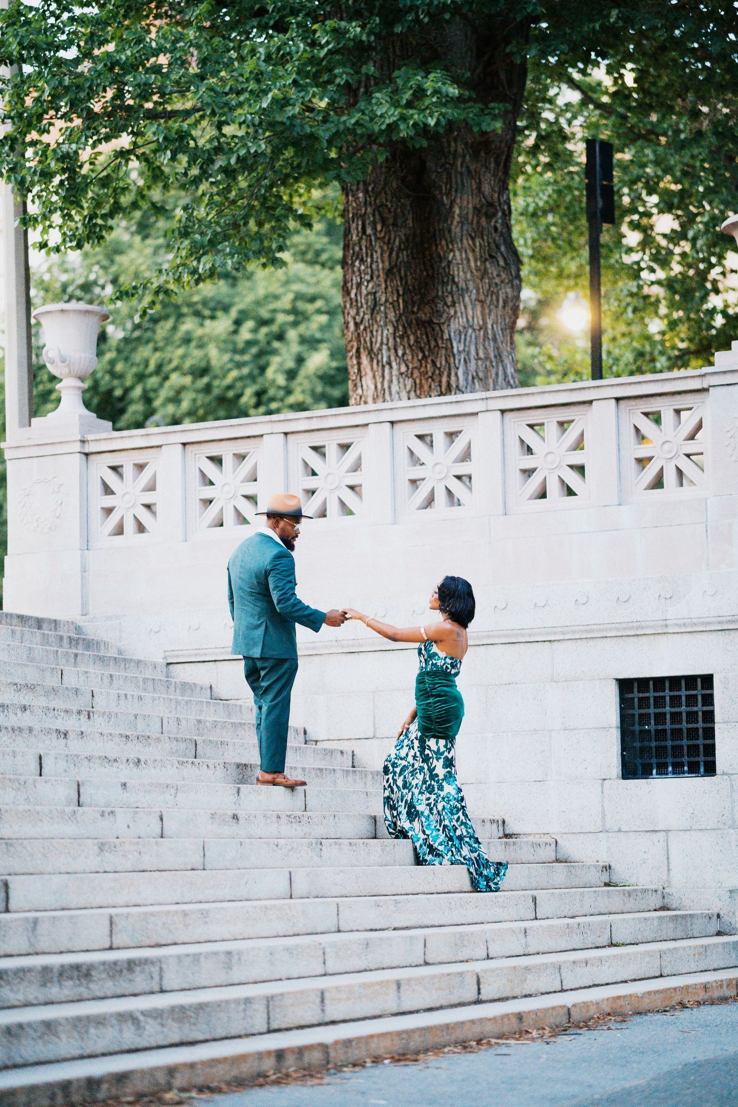 Elegant Black couple holding hands on marble steps outdoors in coordinating green attire.