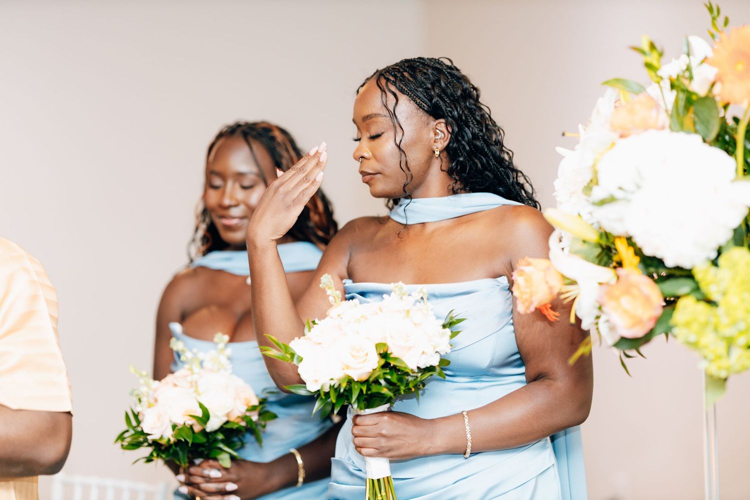 Two bridesmaids in light blue dresses holding white and yellow bouquets during a wedding ceremony.