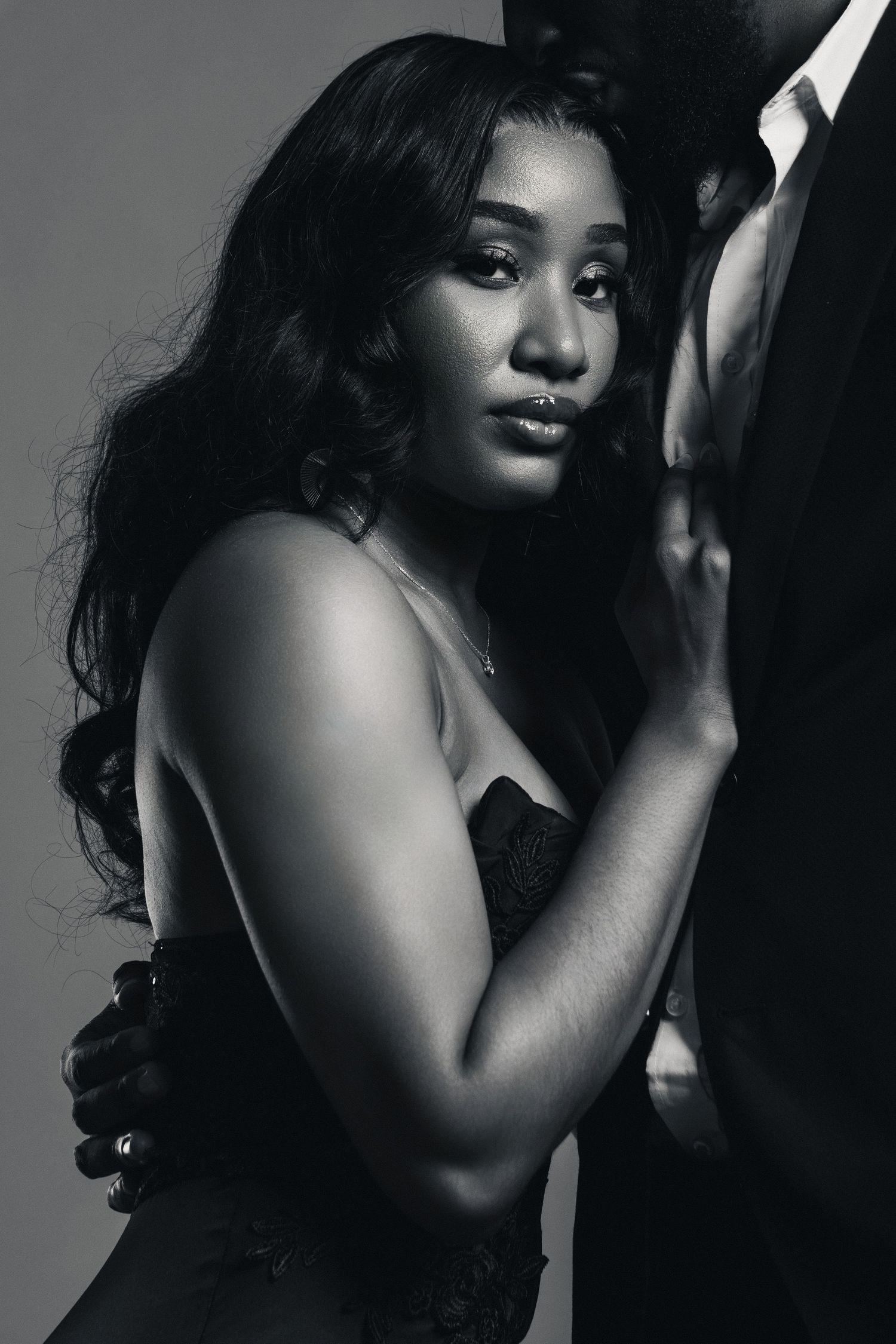 Black and white portrait of a young woman in elegant attire leaning against a man in a suit.
