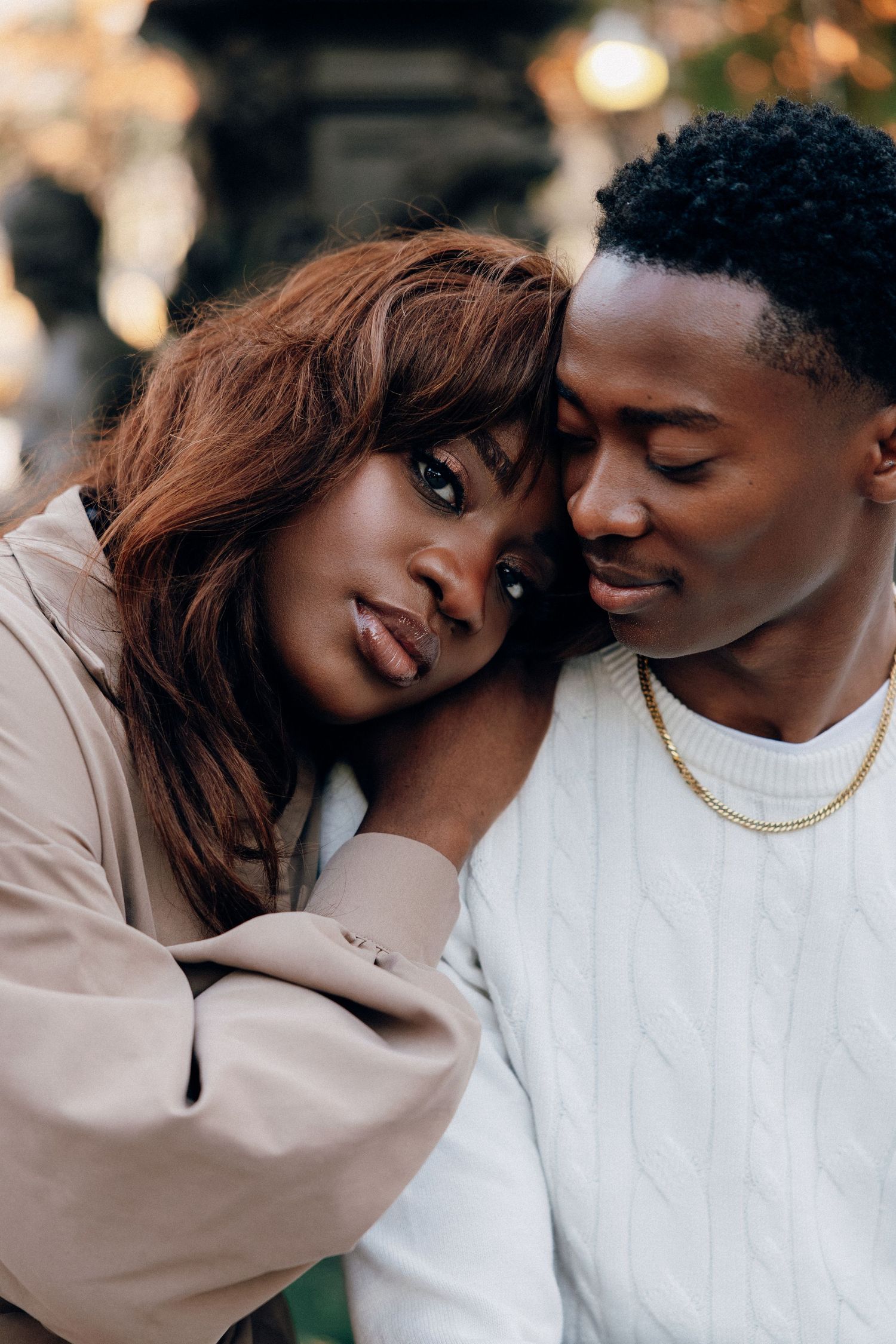 A young Black couple shares a tender moment outdoors, the woman resting her head on the mans shoulder affectionately.