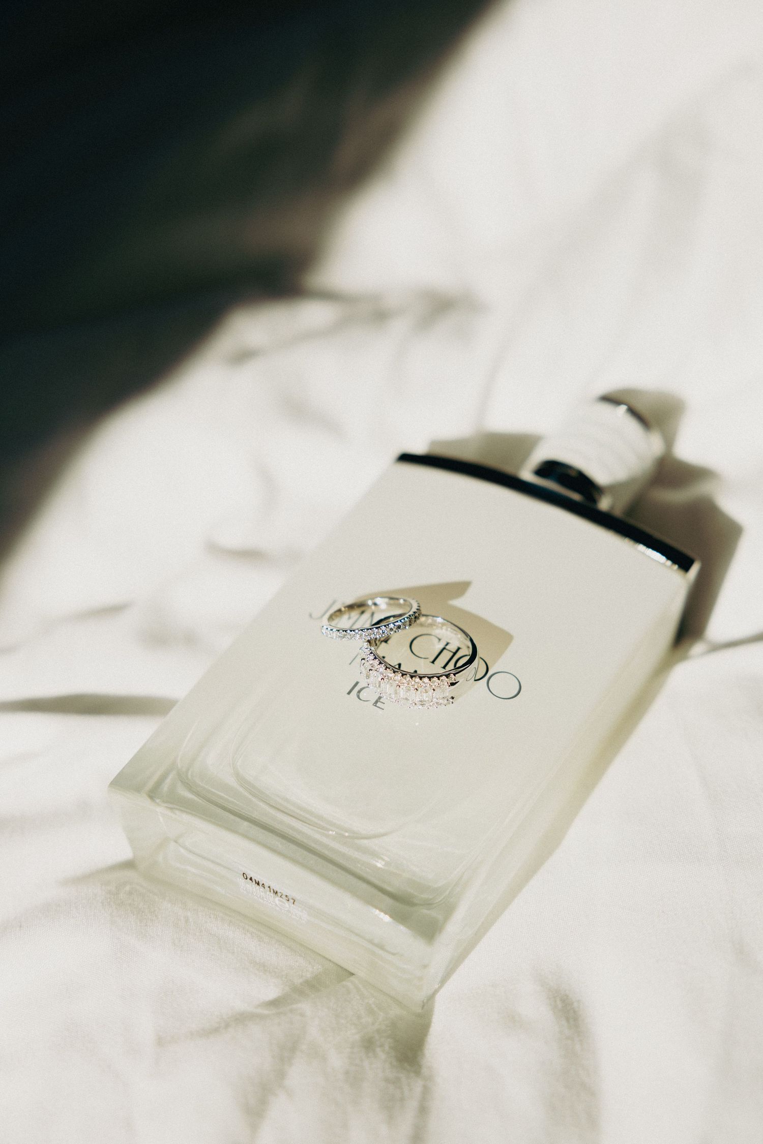 Jimmy Choo Ice perfume bottle on white fabric with diamond wedding rings resting on top.