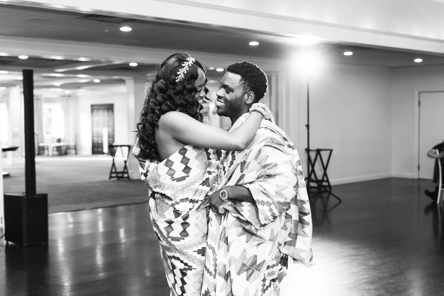 Black and white photo of a couple sharing a romantic dance in traditional African attire at a wedding reception.