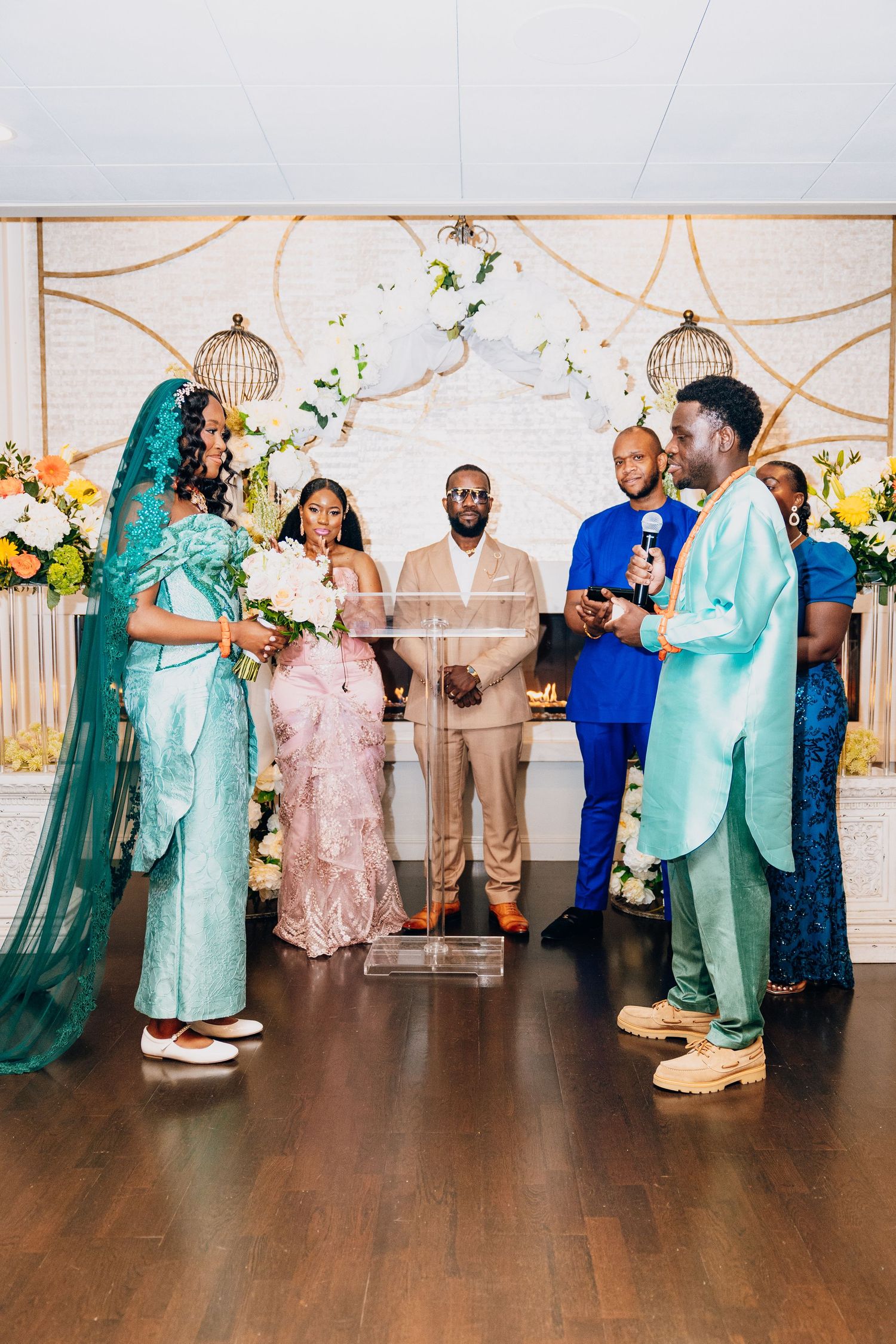 Wedding party stands at altar as officiant reads vows during colorful African-inspired ceremony.