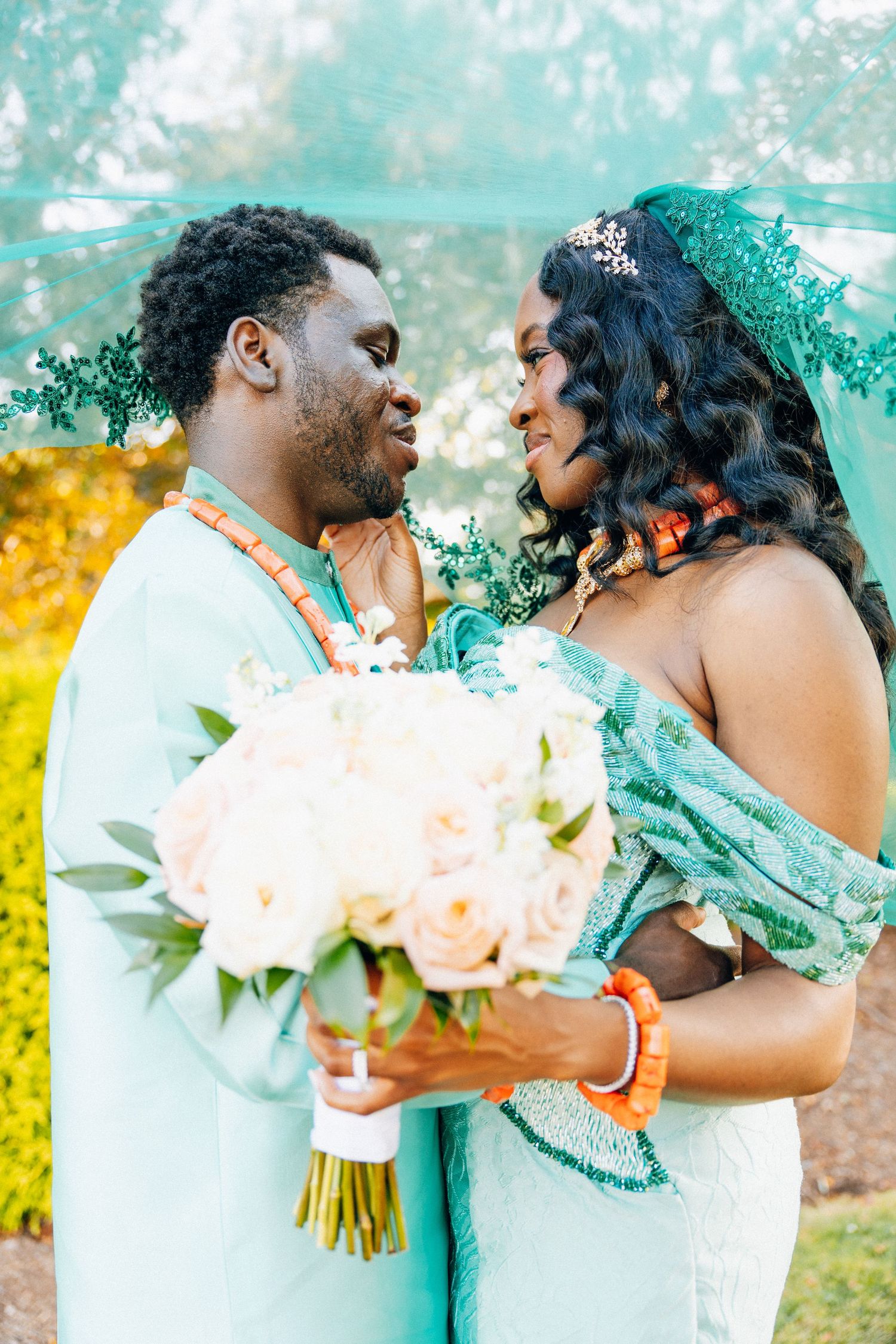 African couple in matching teal traditional attire share romantic moment with bouquet.