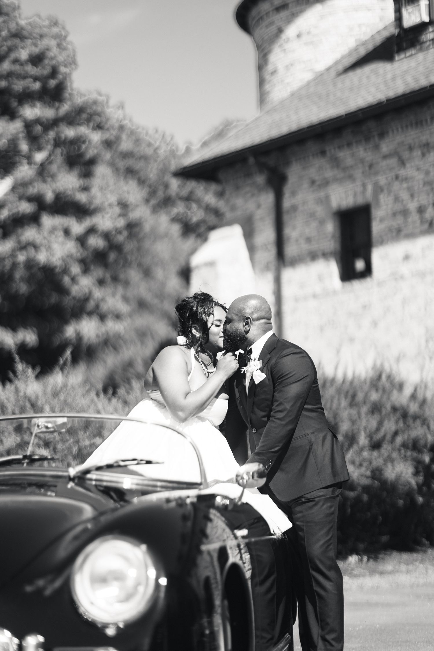 Black and white photo of bride and groom sharing a kiss beside a vintage Porsche.