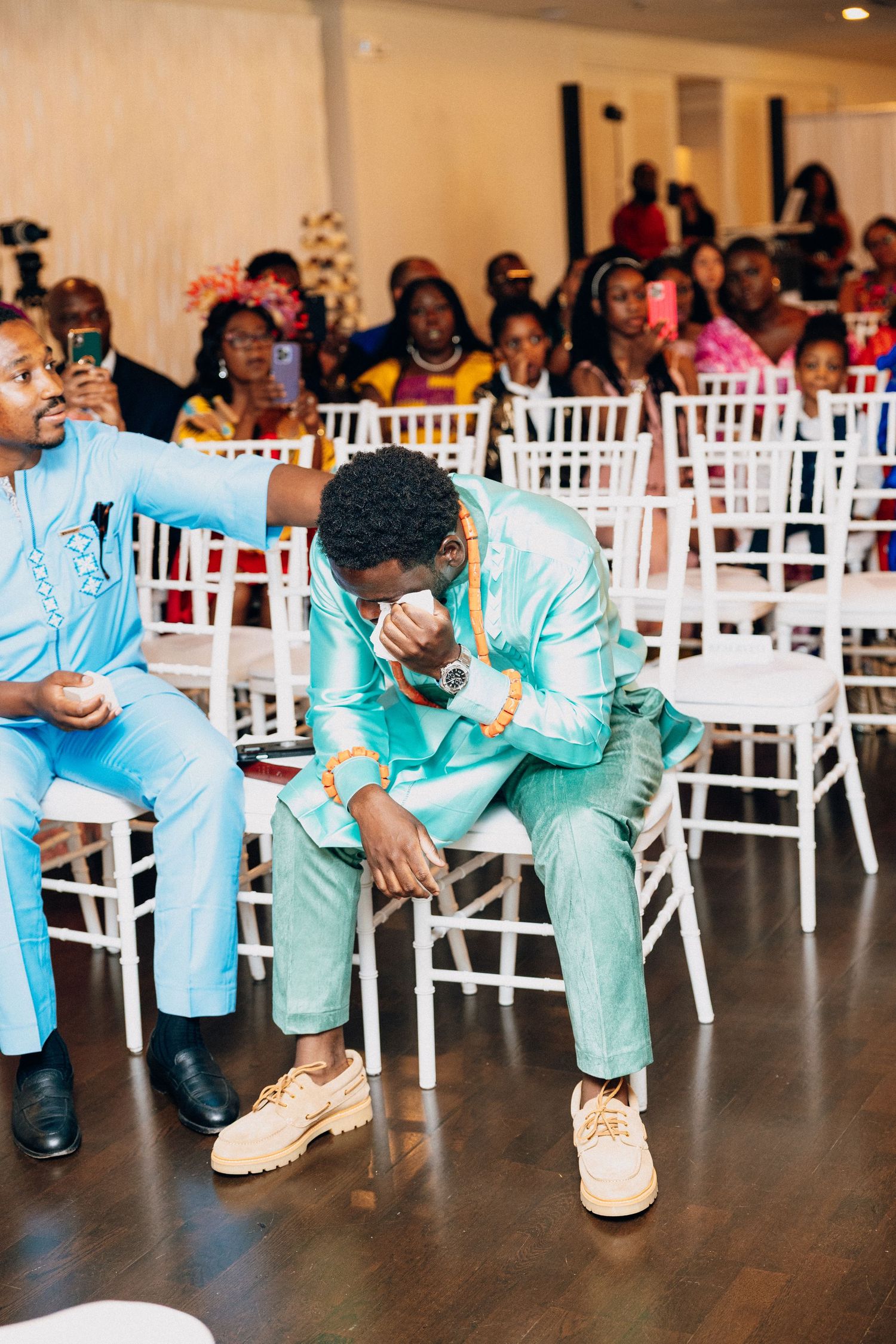 Emotional groom in mint green African attire wipes tears during wedding ceremony.