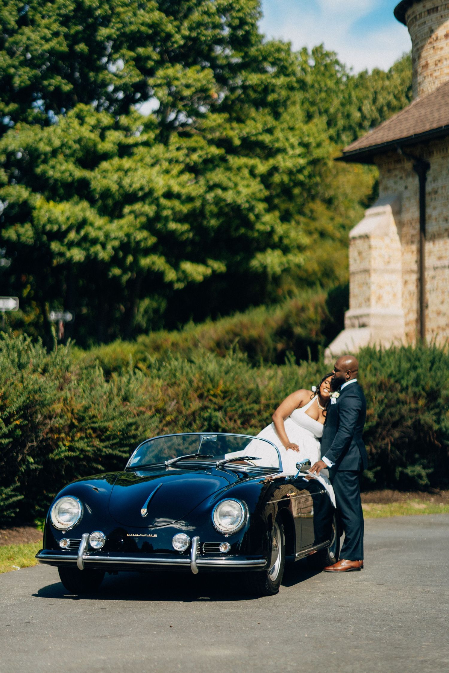 Bride and groom posing with a classic vintage navy blue Porsche 356 convertible on their wedding day.