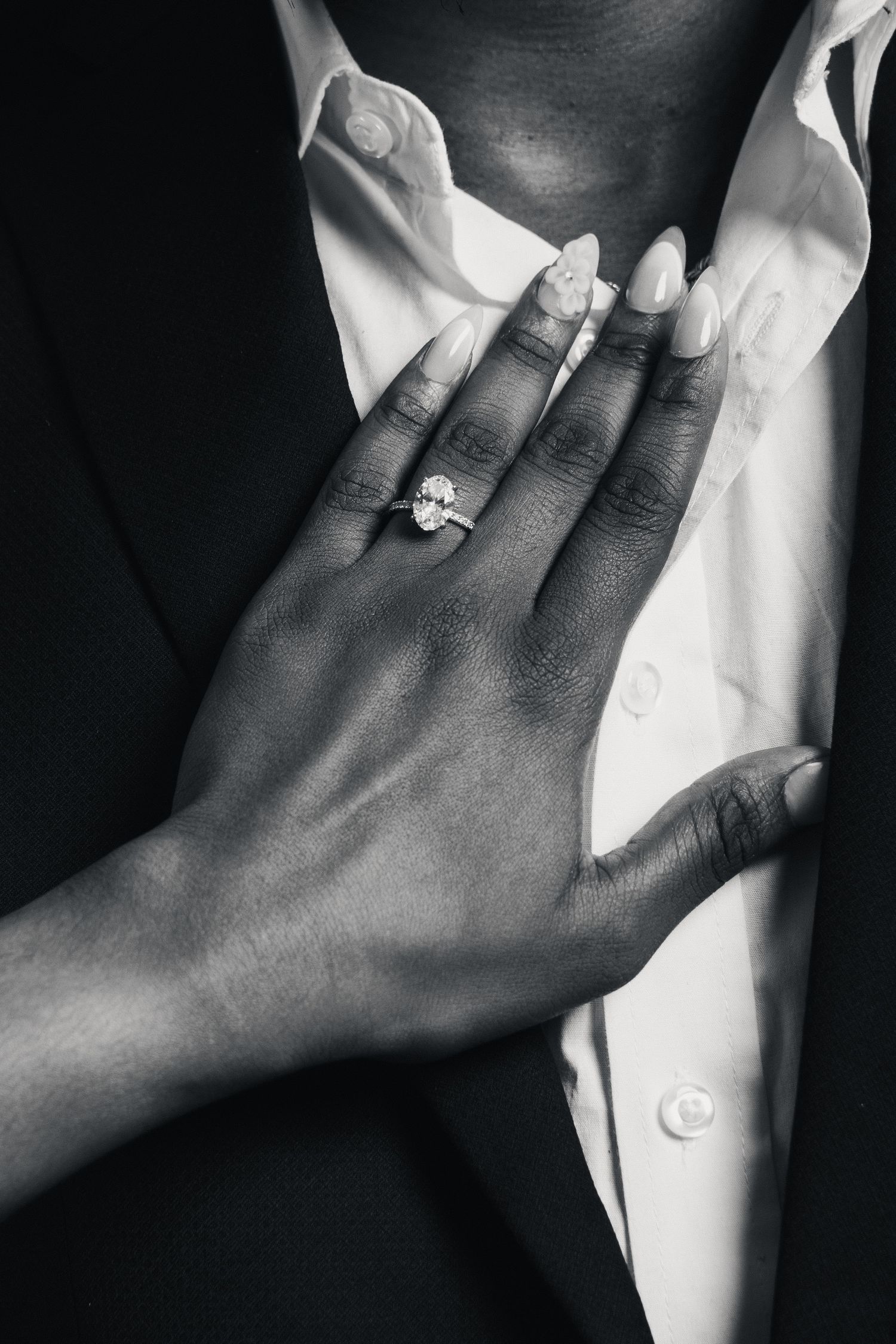 Black and white photo of a woman's hand with a diamond engagement ring resting on a man's white dress shirt.