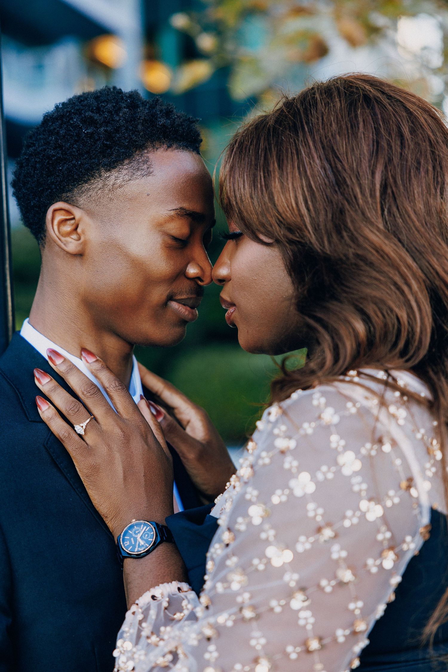 Two people sharing a romantic moment, nearly kissing, dressed elegantly with a watch and ring visible.