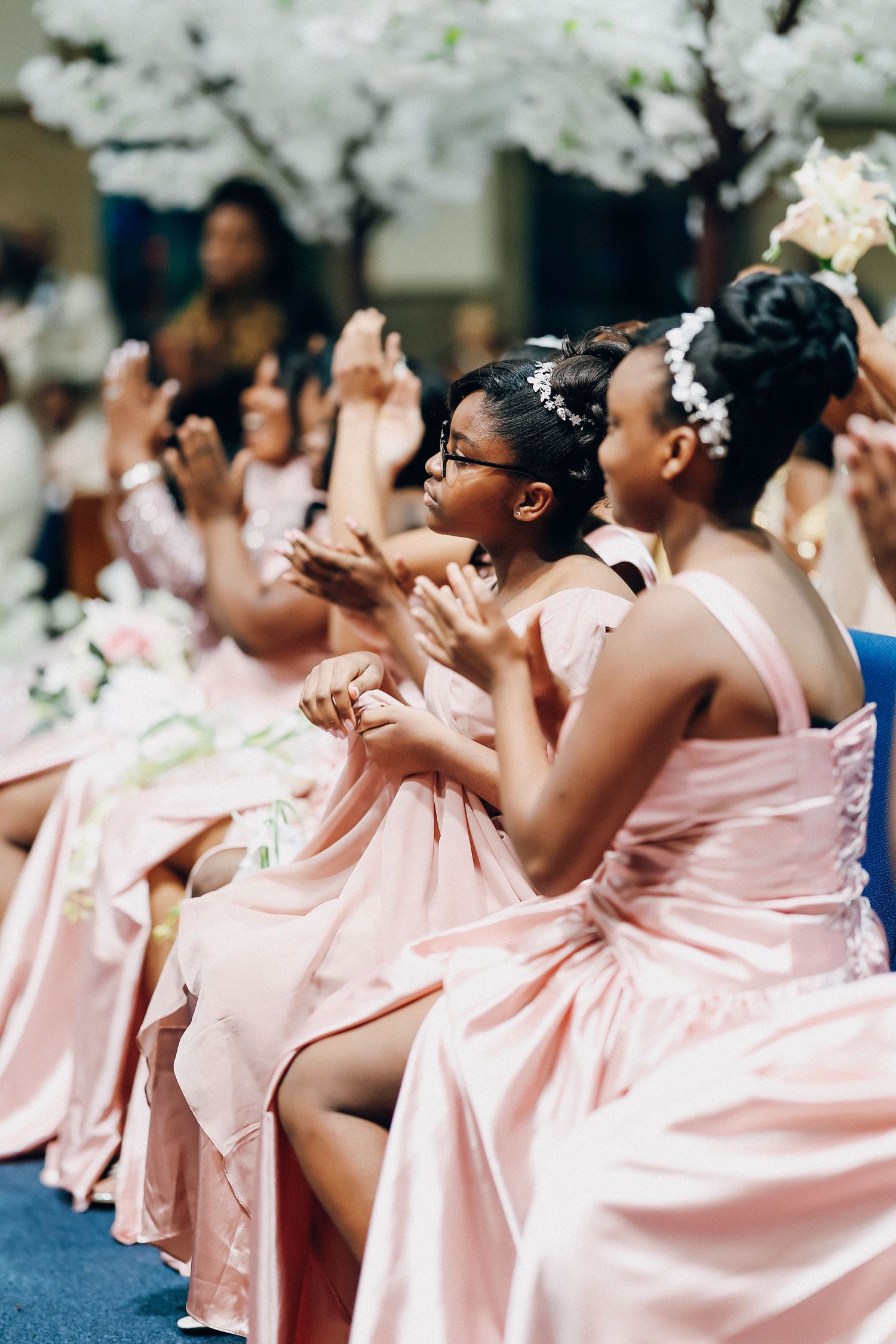 Bridesmaids in pink satin dresses clapping during wedding ceremony.