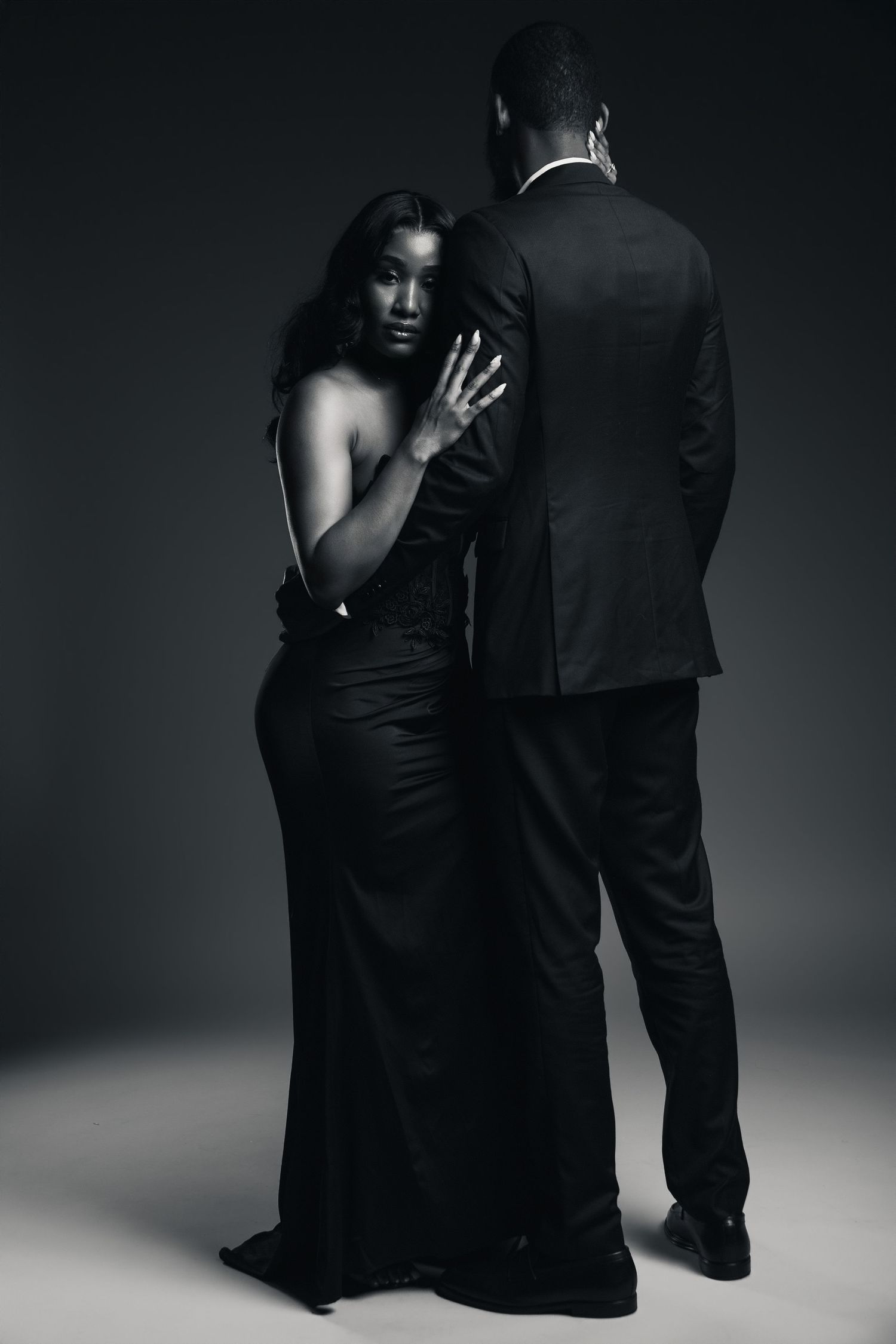 Elegant black and white photo of a couple in formal attire, woman in gown leaning against man in suit.