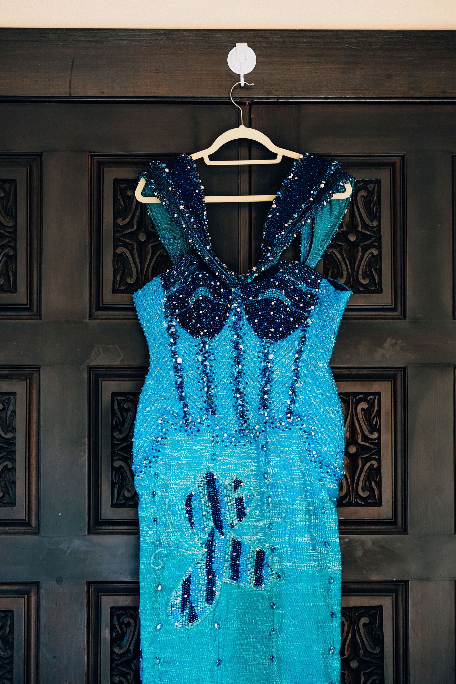 Stunning turquoise sequined gown with navy beaded embellishments hanging on a wooden door hanger.