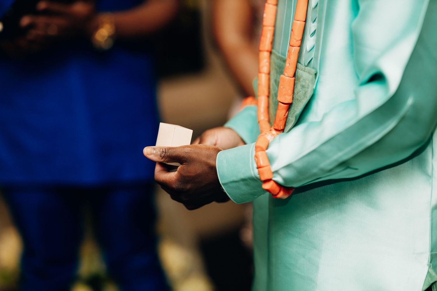Man in mint green traditional African attire holding a small white card at a cultural ceremony.