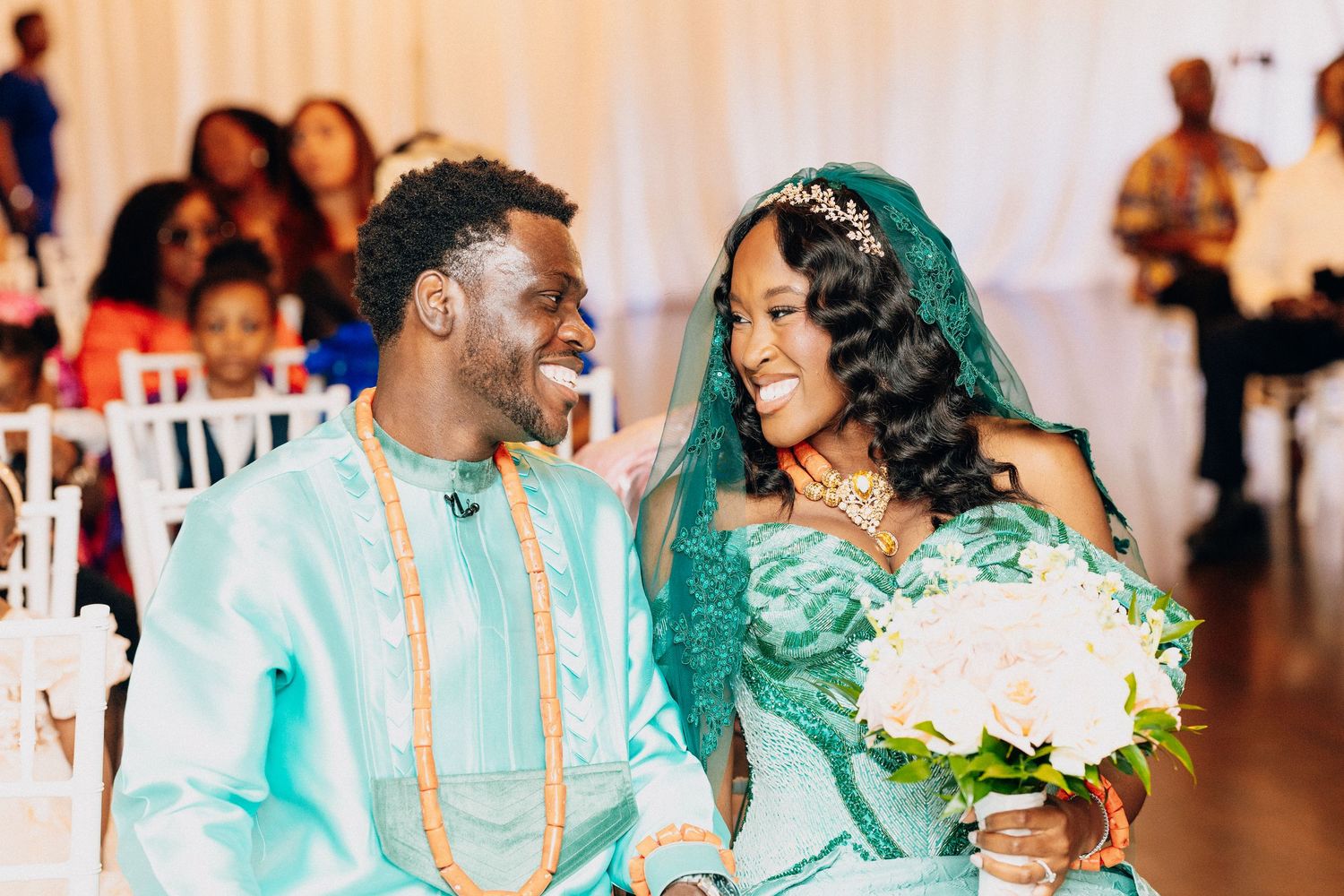 Smiling bride and groom in matching teal African traditional wedding attire share a joyful moment.