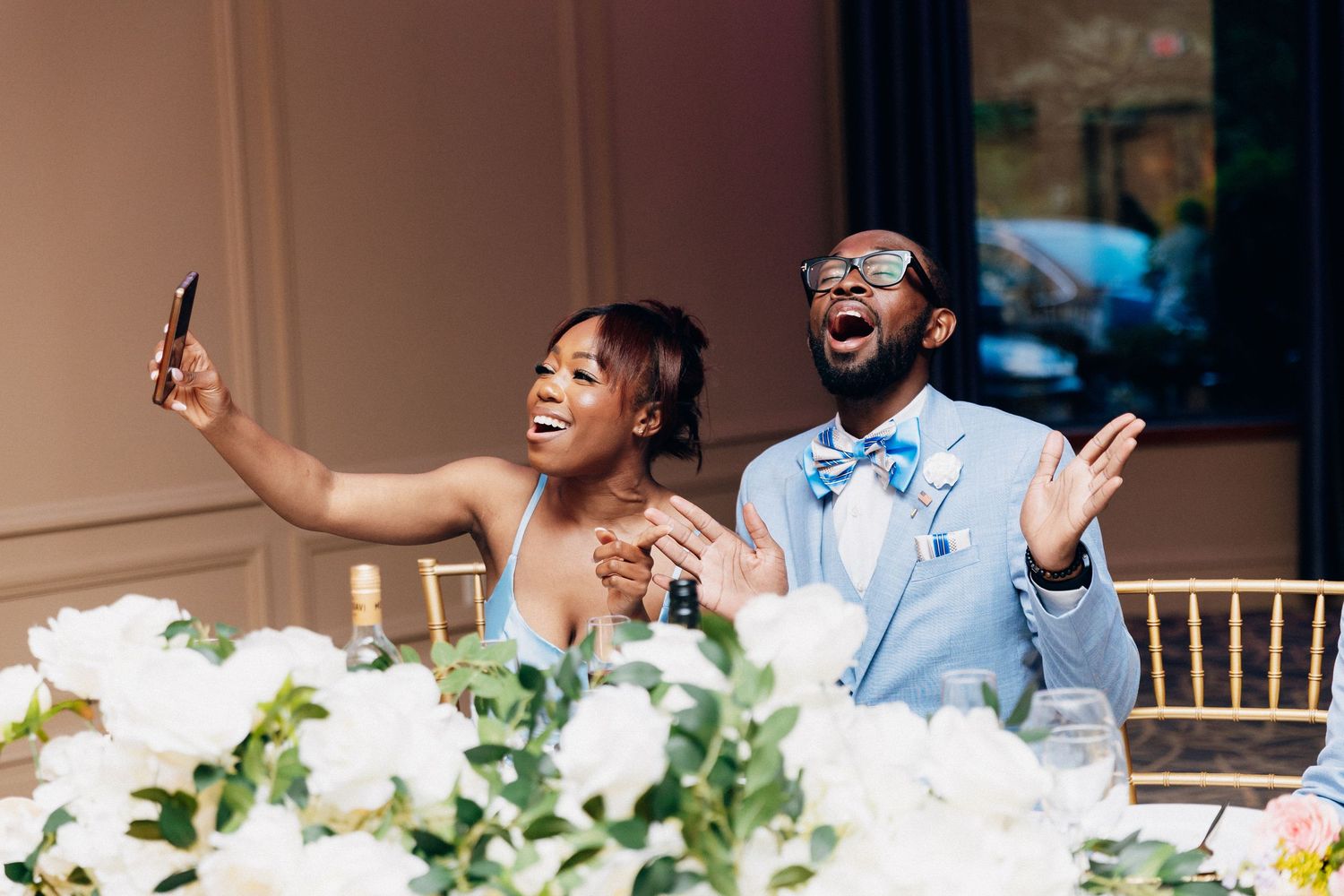 Happy newlywed couple taking a selfie at their wedding reception, laughing and celebrating at the head table.