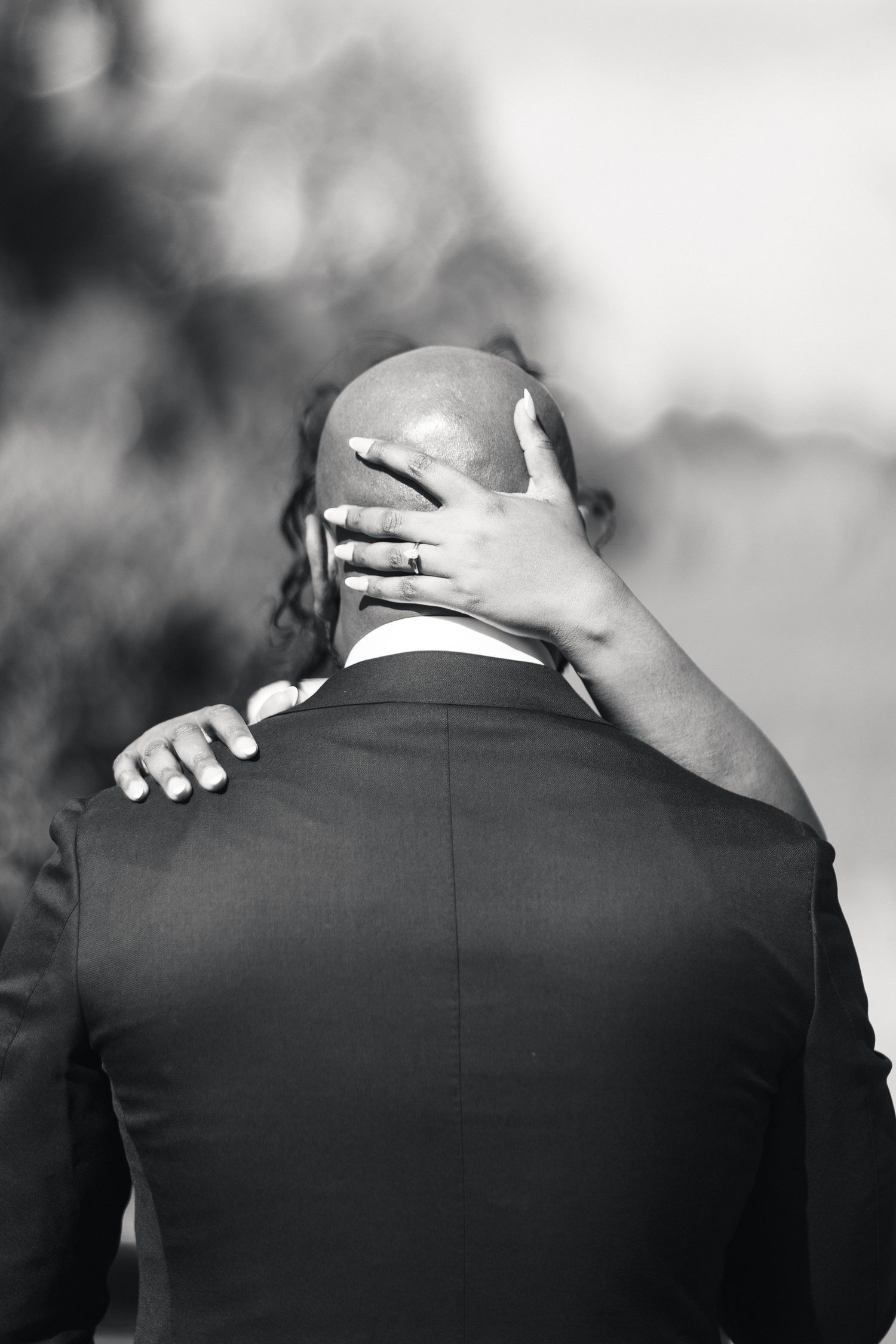 Black and white photo of bride placing hand on bald groom's head from behind in tender moment.