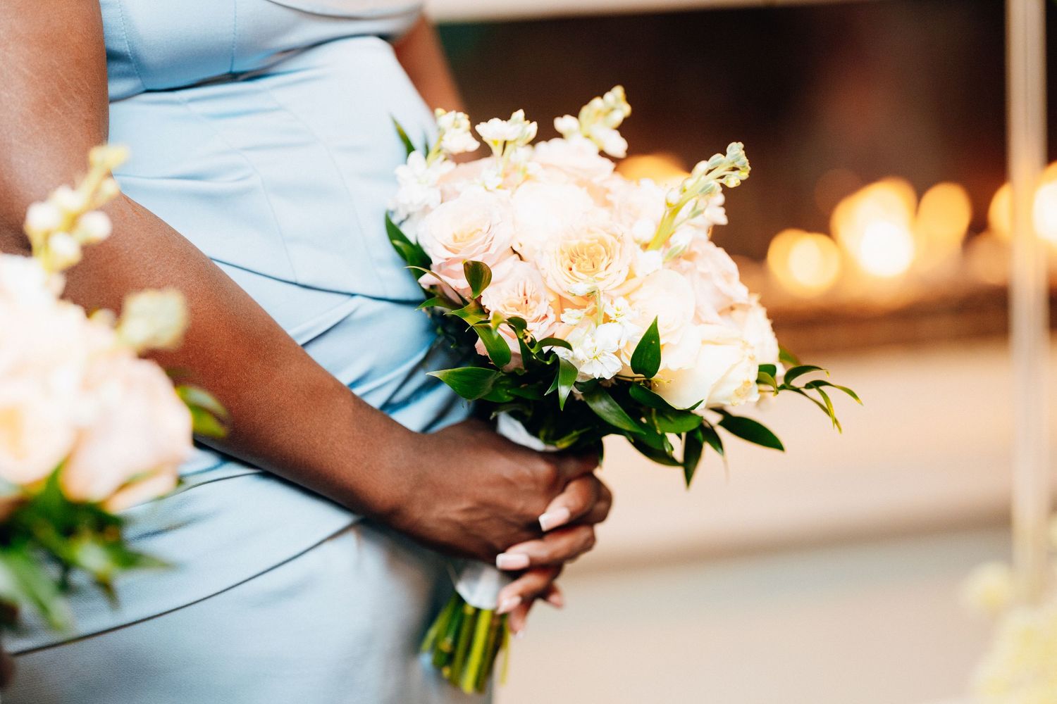 Bridesmaid in light blue dress holding a elegant white and peach wedding bouquet with greenery.
