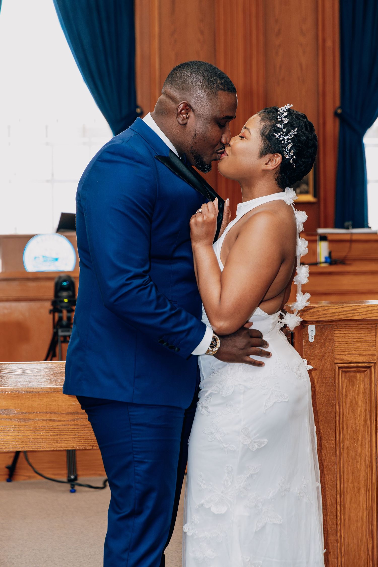 A bride and groom share a first kiss during their wedding ceremony inside a wood-paneled courthouse.