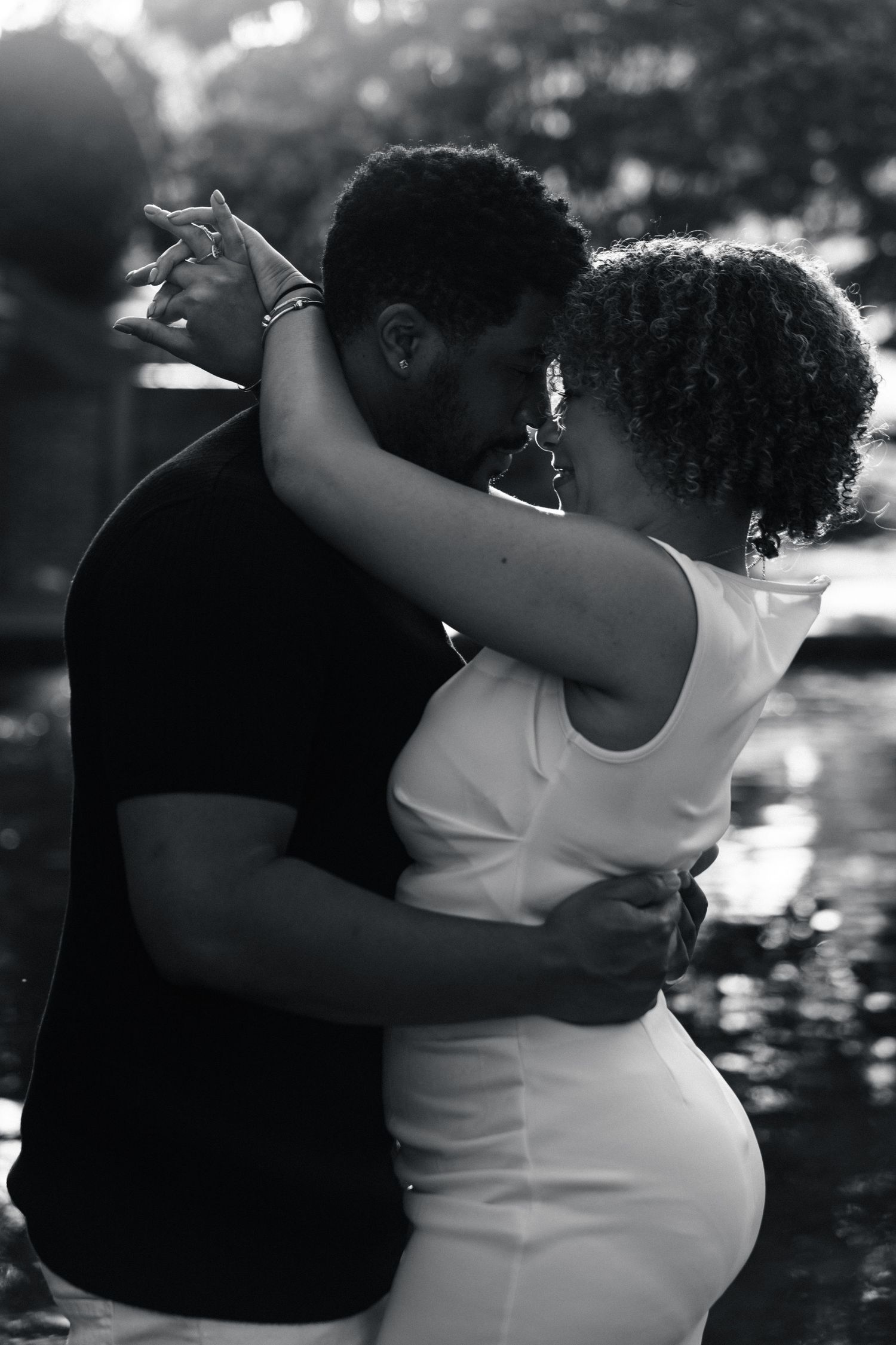 Black and white romantic photo of a couple holding hands and embracing near a reflective pond.