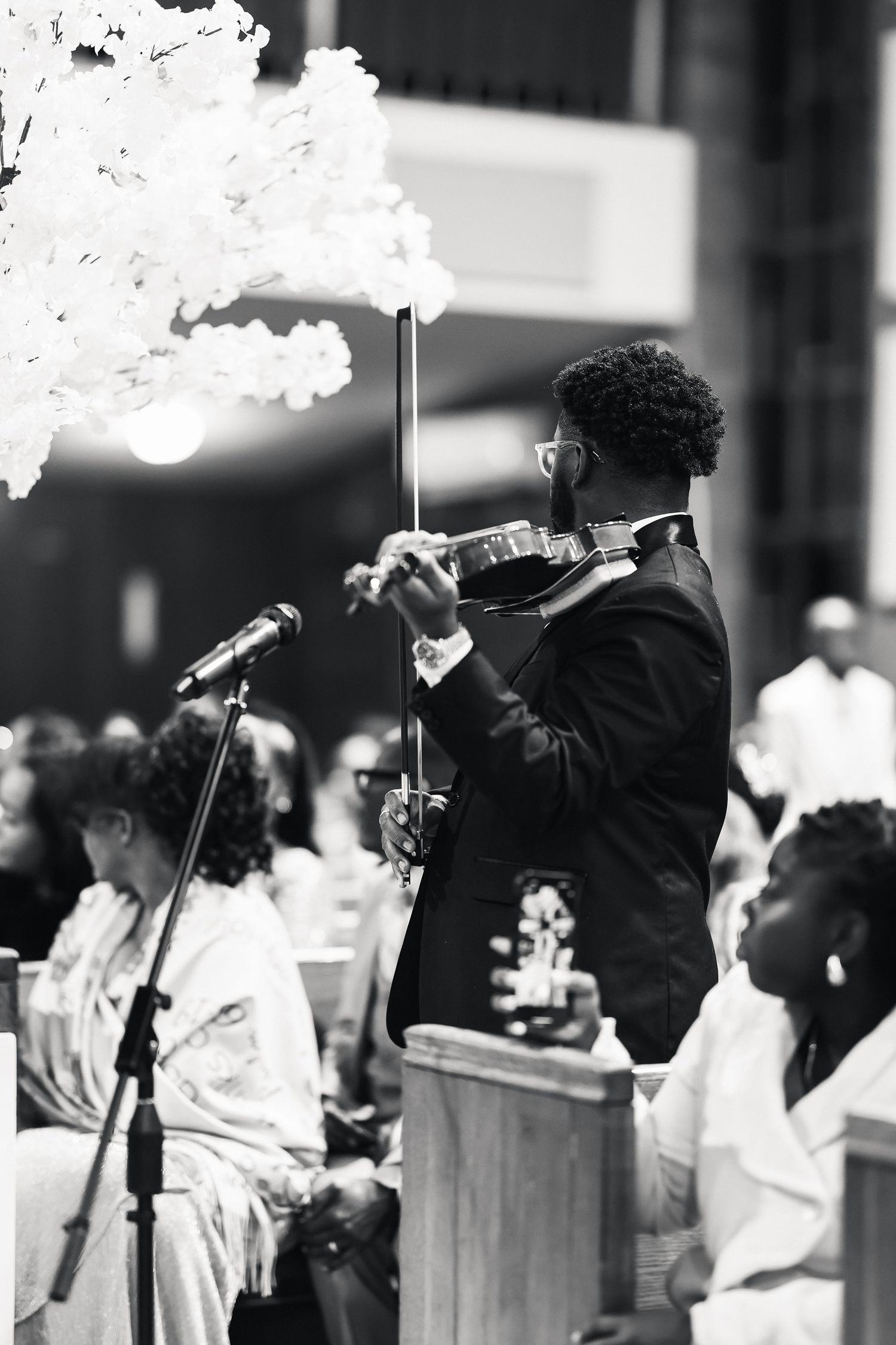 Black and white photo of a violinist performing at a church wedding ceremony with guests seated in pews.