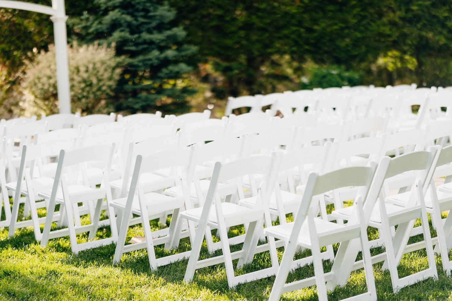 Rows of white folding chairs set up on green grass for an outdoor wedding ceremony.