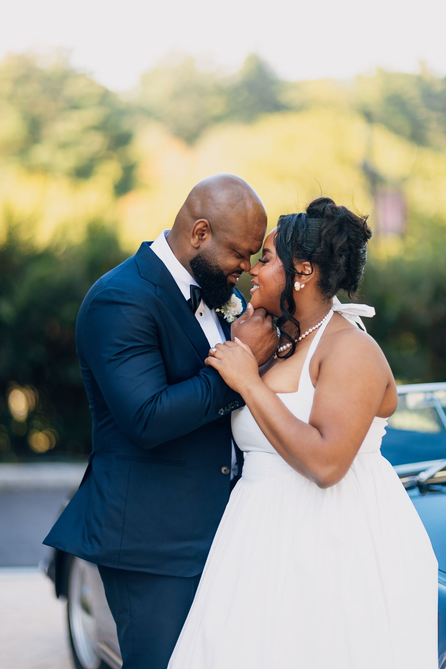 Newlyweds share an intimate moment, nearly kissing, with golden bokeh trees in the background.