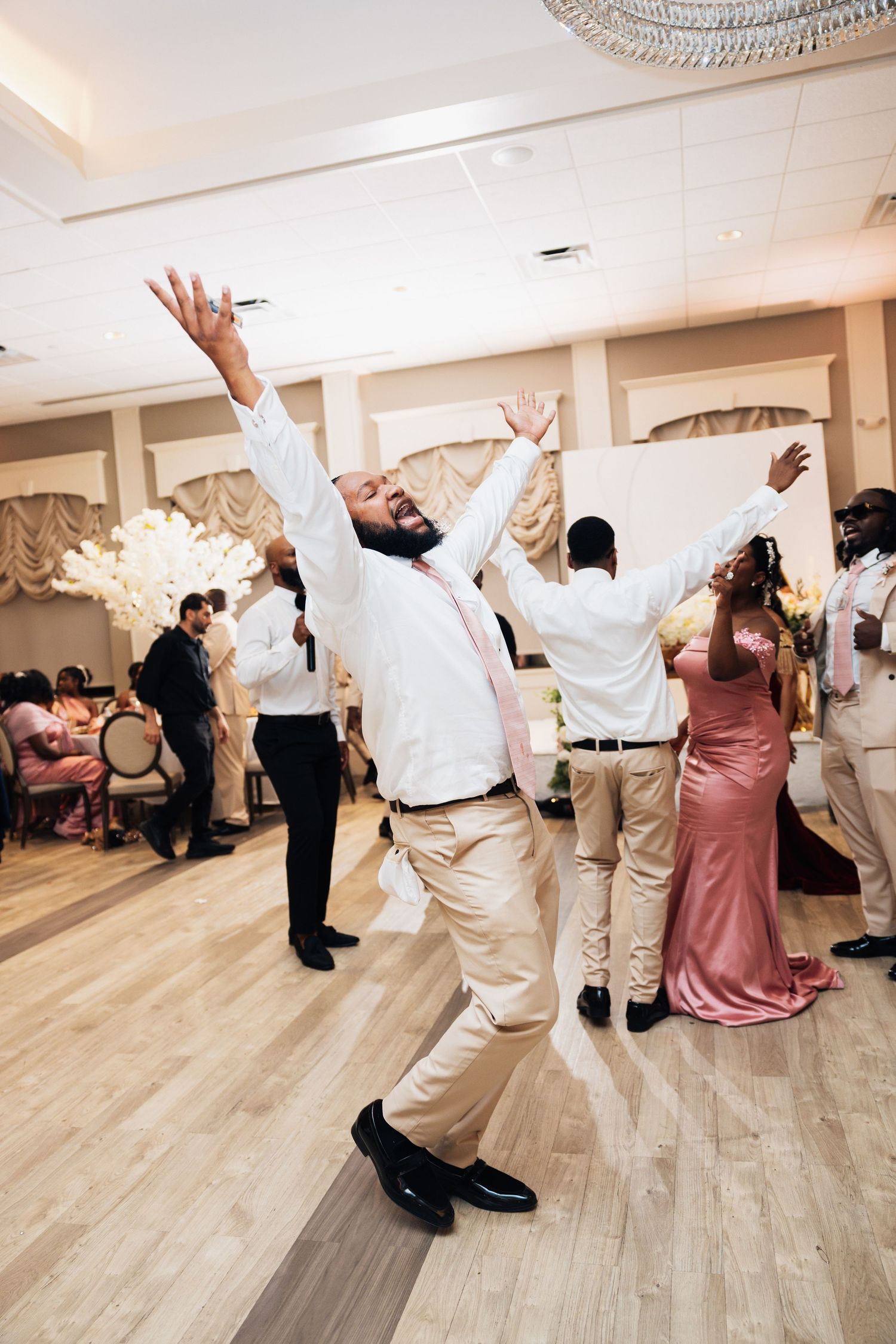 Joyful wedding guest dances with arms raised on dance floor during lively wedding reception celebration.