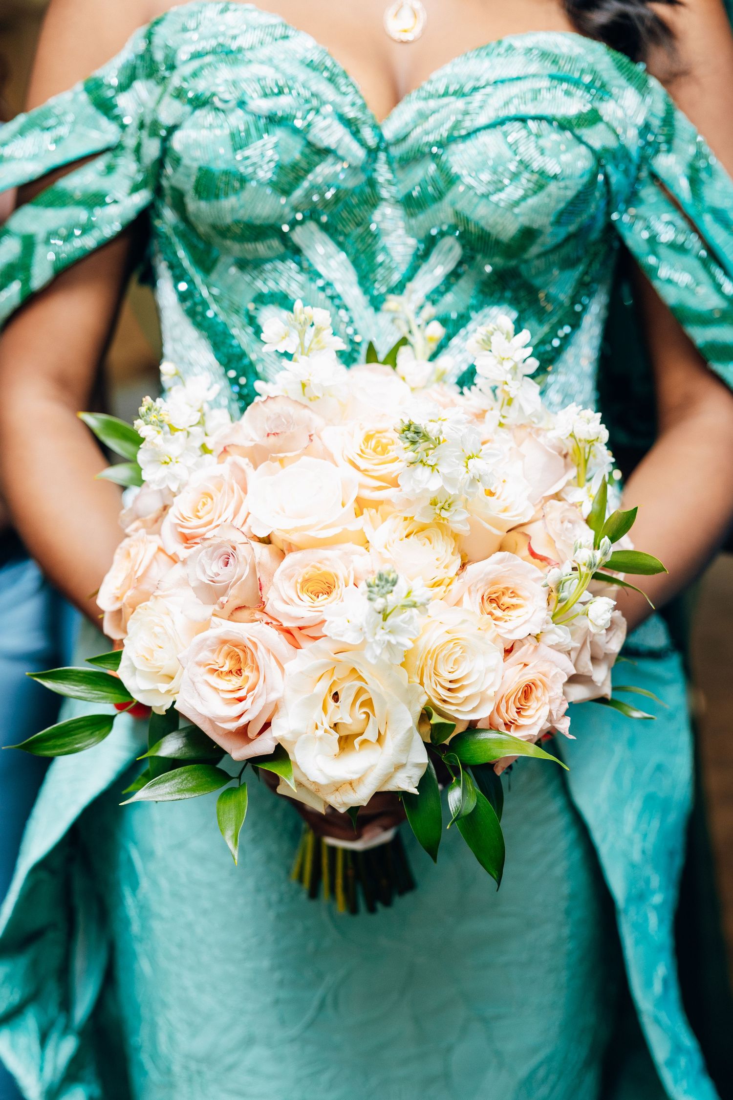 Bride holding a lush bouquet of peach and white roses in a teal sequined gown.