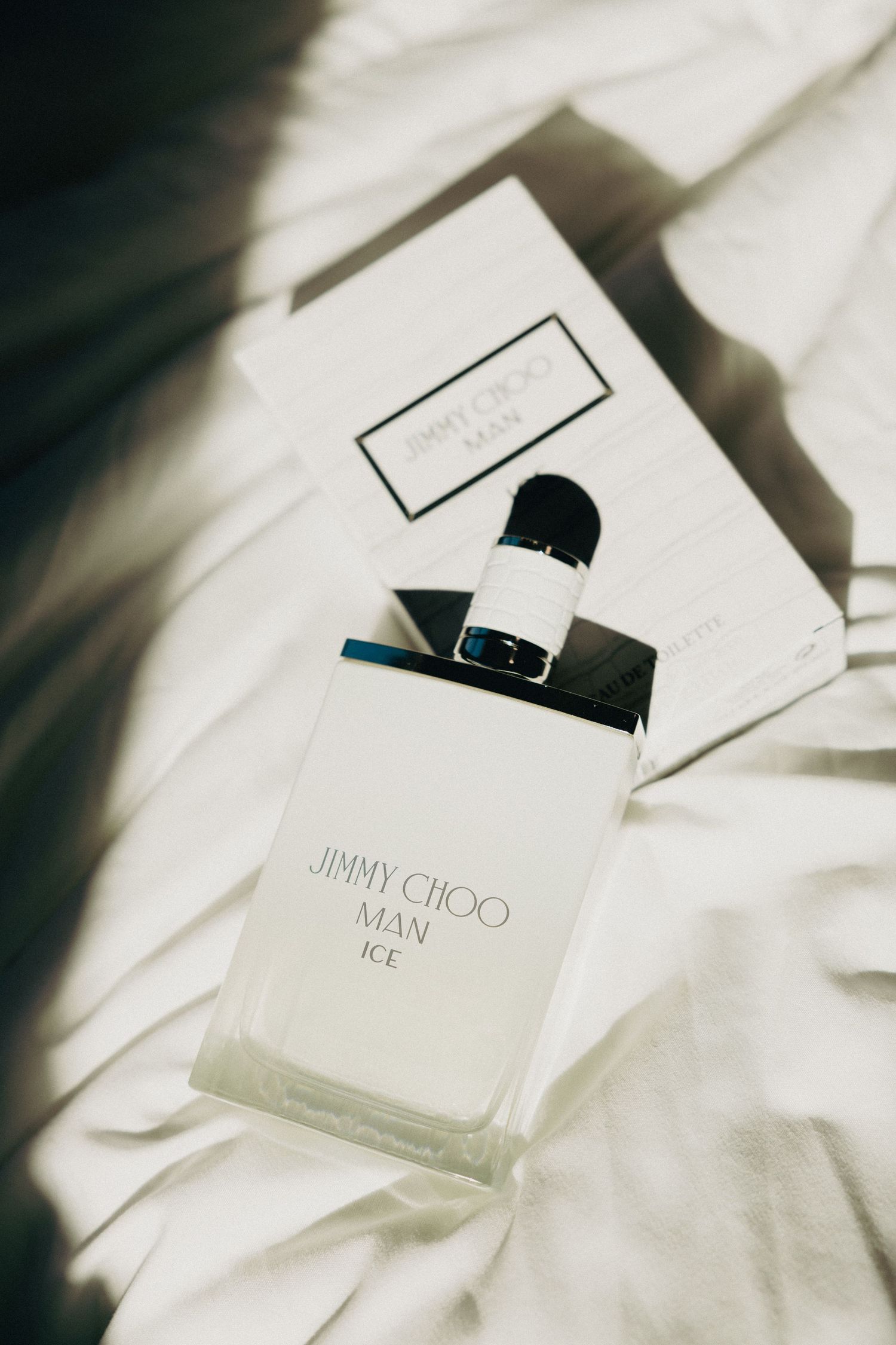 Jimmy Choo Man Ice cologne bottle and box resting on white fabric in soft natural light.