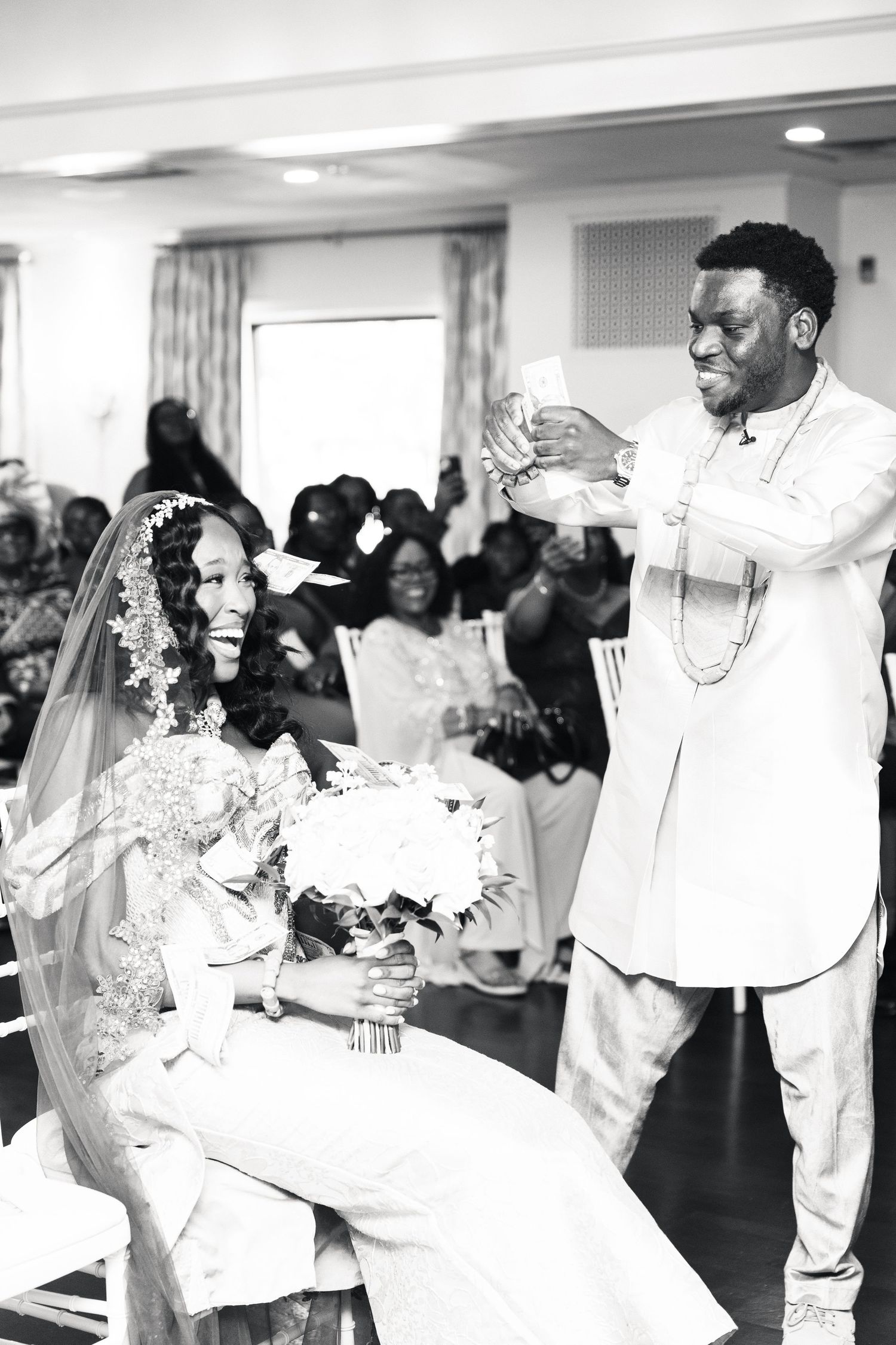 Black and white photo of groom sprinkling money on smiling bride at traditional African wedding.