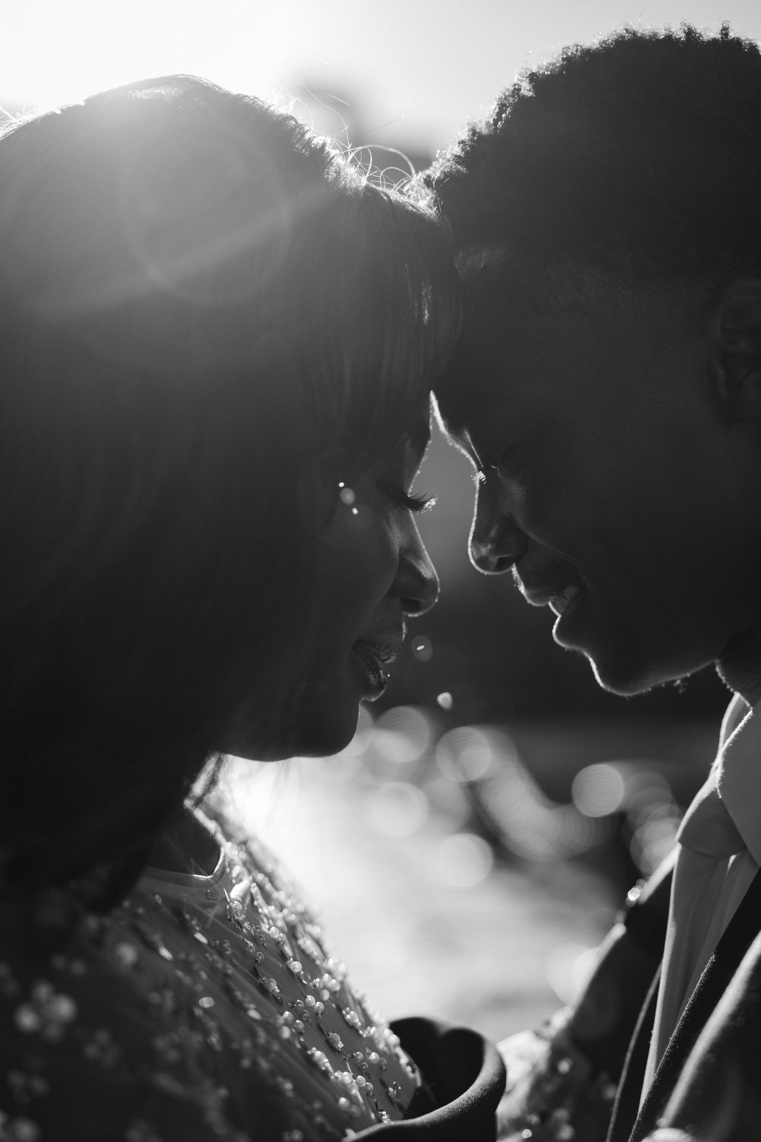 Black and white romantic photo of couple facing each other with sunlight glowing behind them.