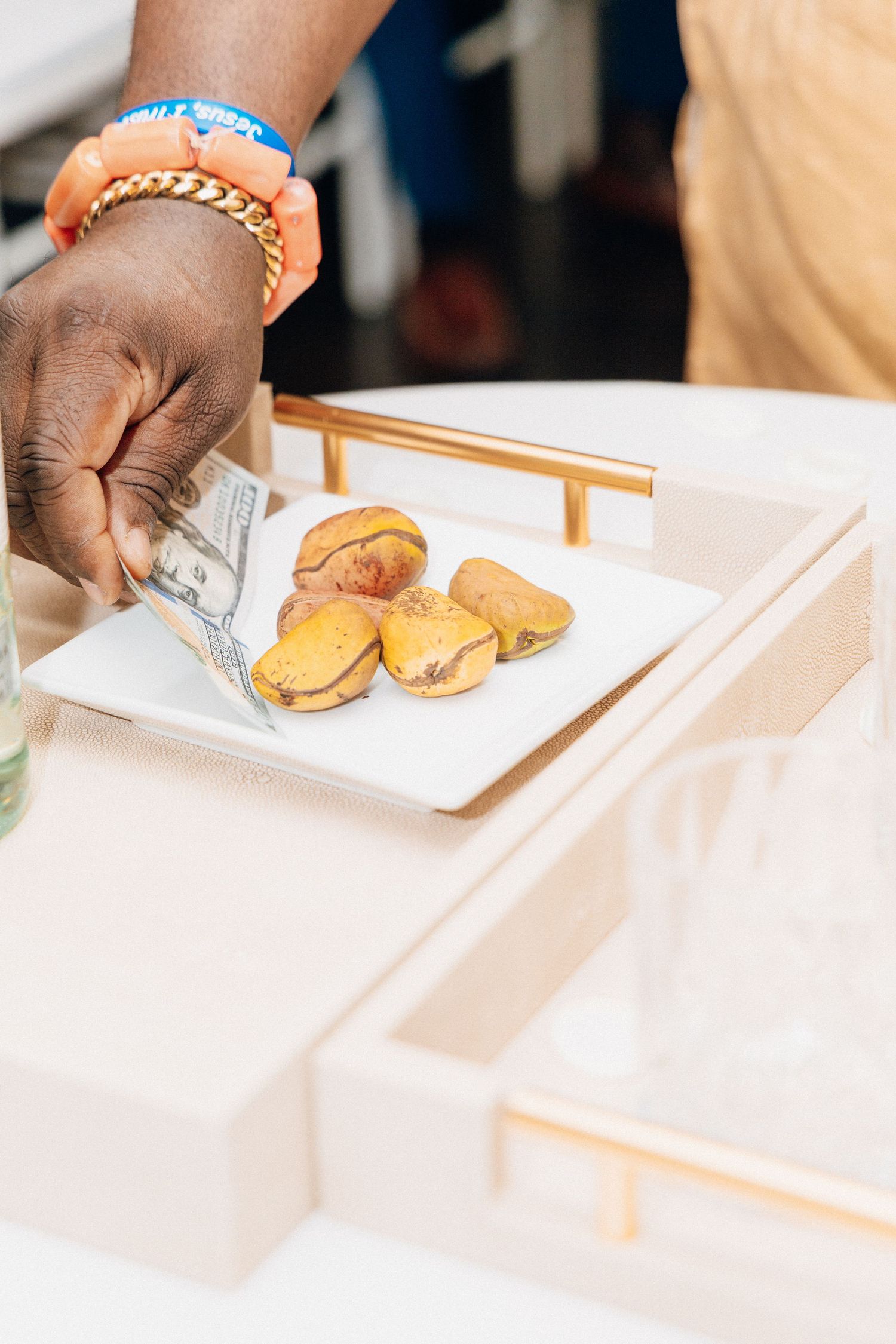 A hand with gold bracelet and wristband places money on a white plate with golden pastries on a elegant tray.