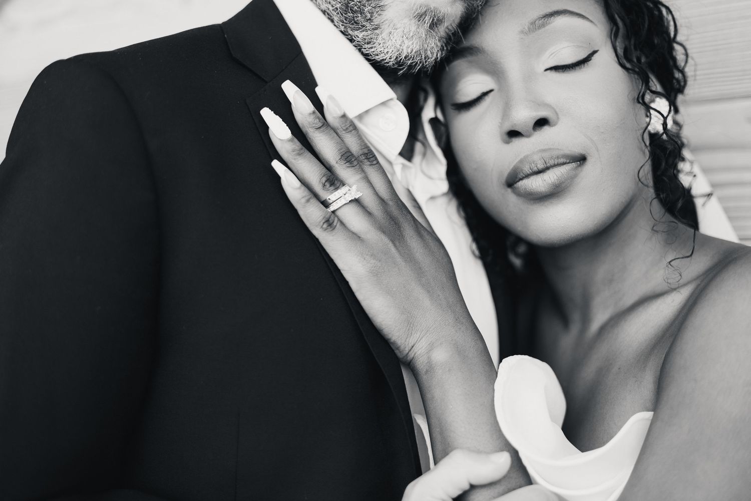 Black and white photo of bride and groom in tender embrace, bride showing diamond engagement ring.