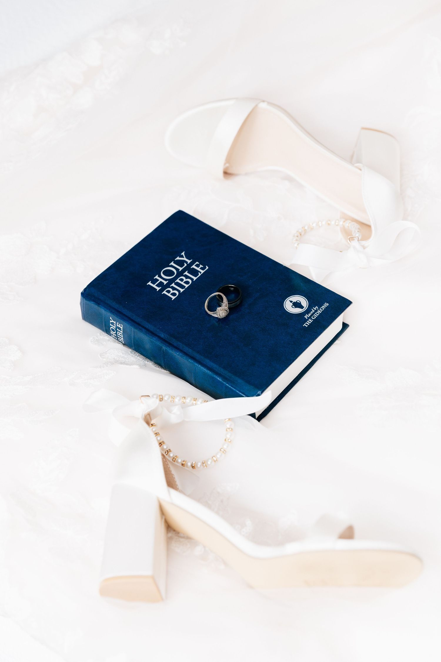White block heel bridal shoes, pearl necklace, and wedding ring on a Holy Bible.