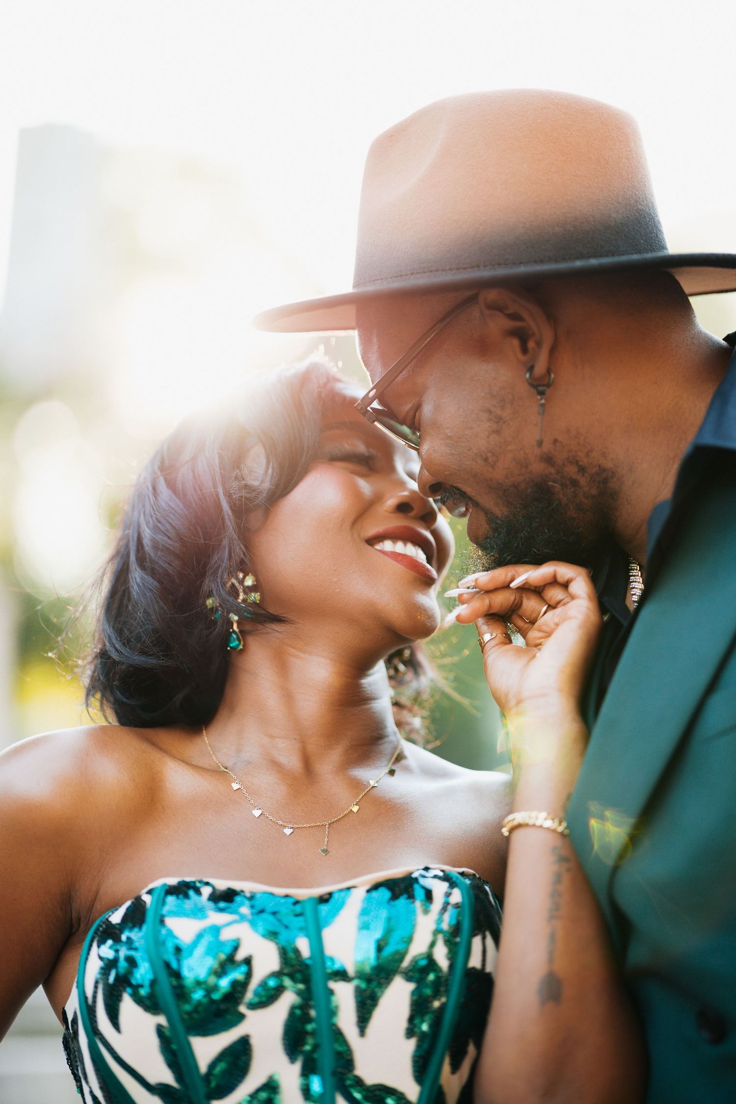 Close-up of smiling couple in teal formal wear sharing romantic moment outdoors.