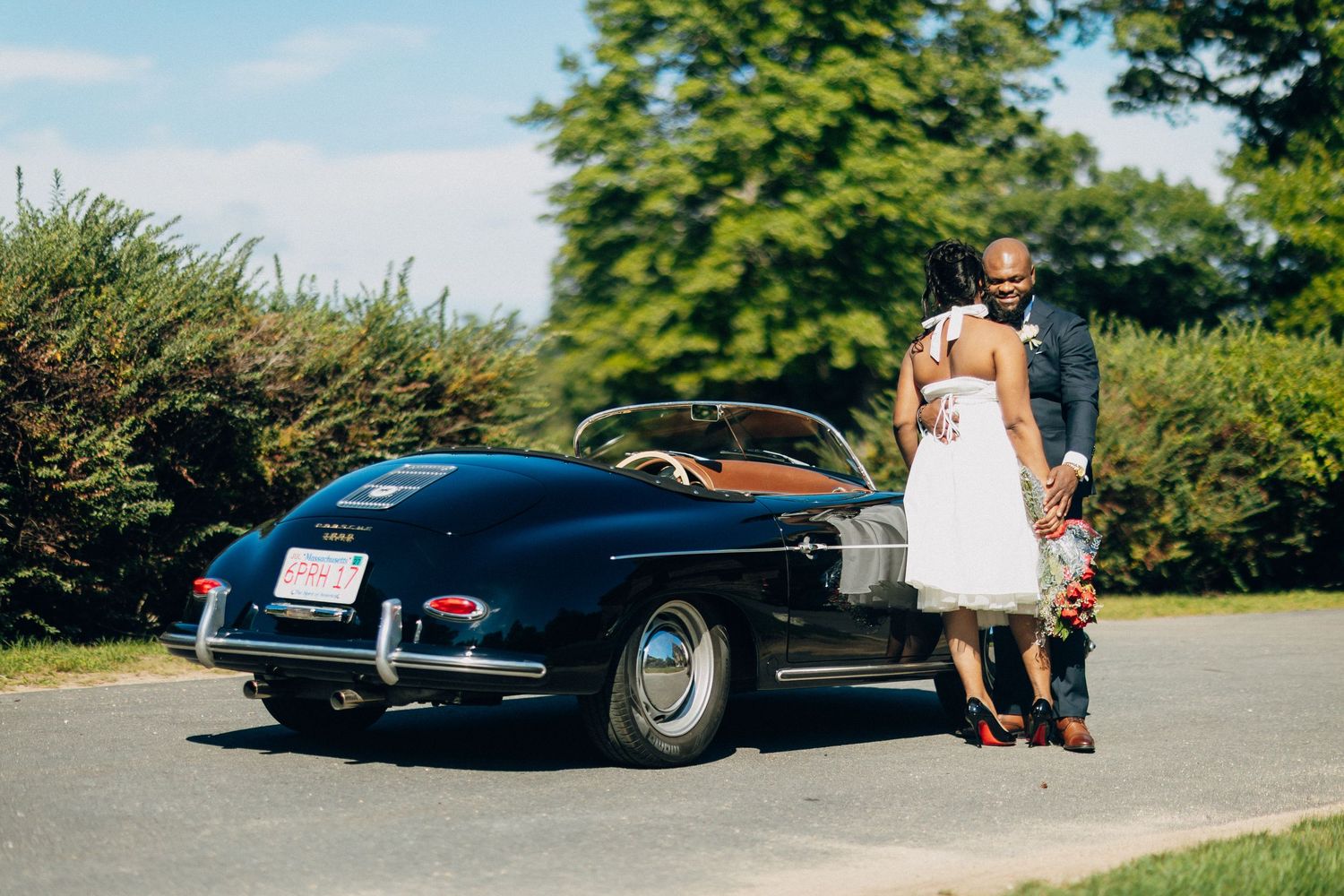 Bride and groom walking toward a classic black vintage convertible on their wedding day.