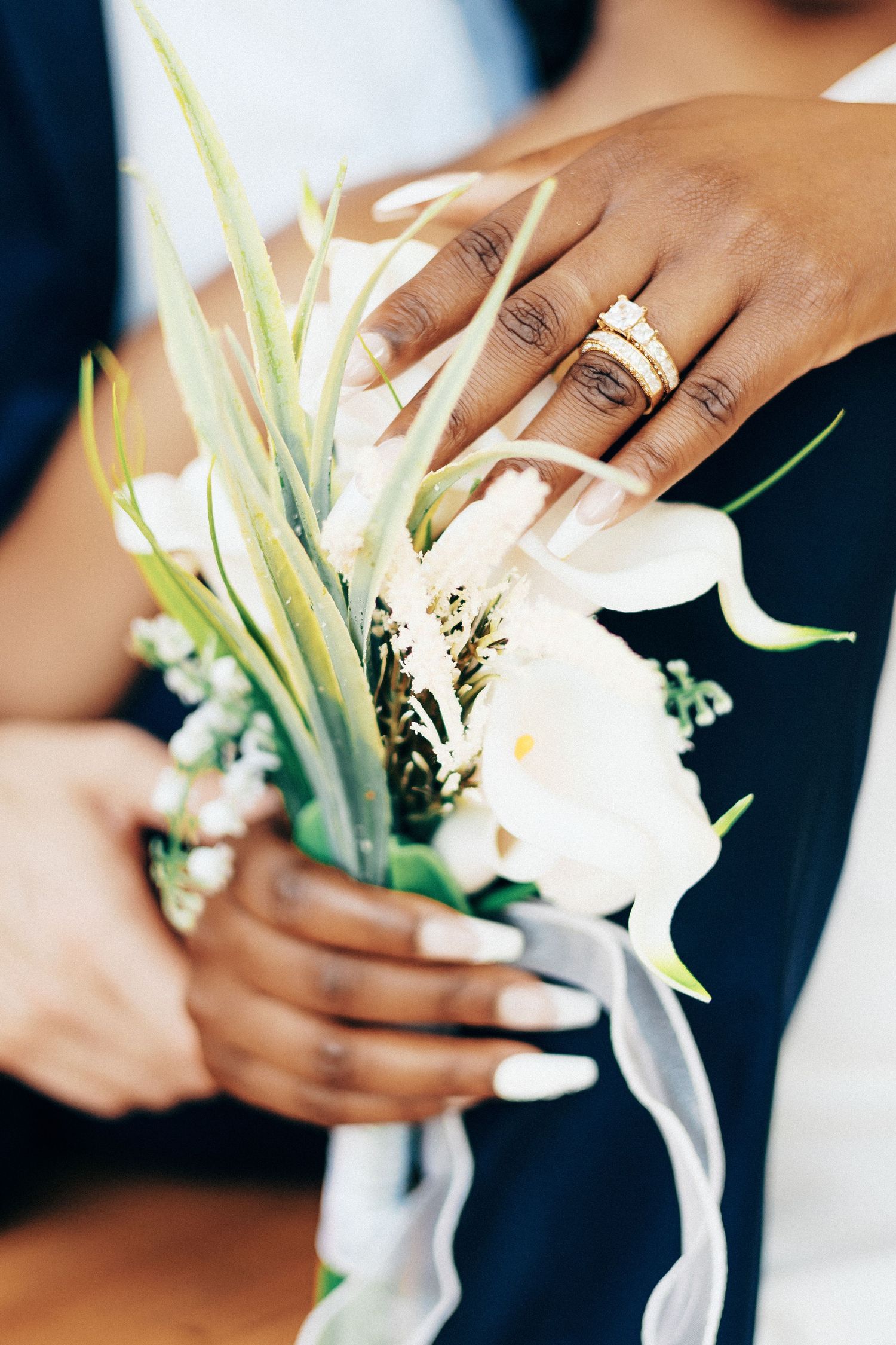 Bride with diamond wedding rings holding elegant white calla lily bouquet with ribbon.