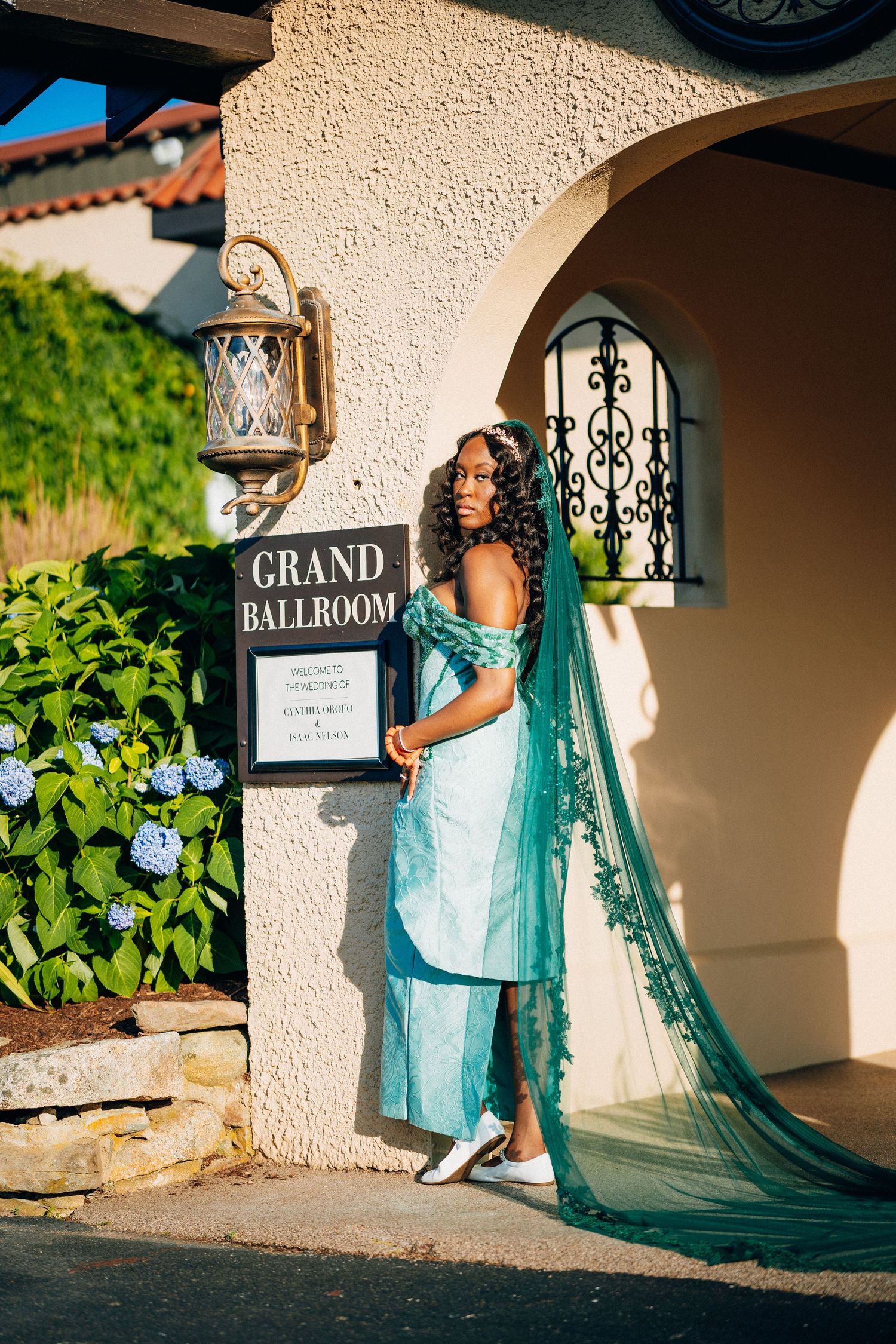 African bride in teal gown stands by Grand Ballroom entrance.