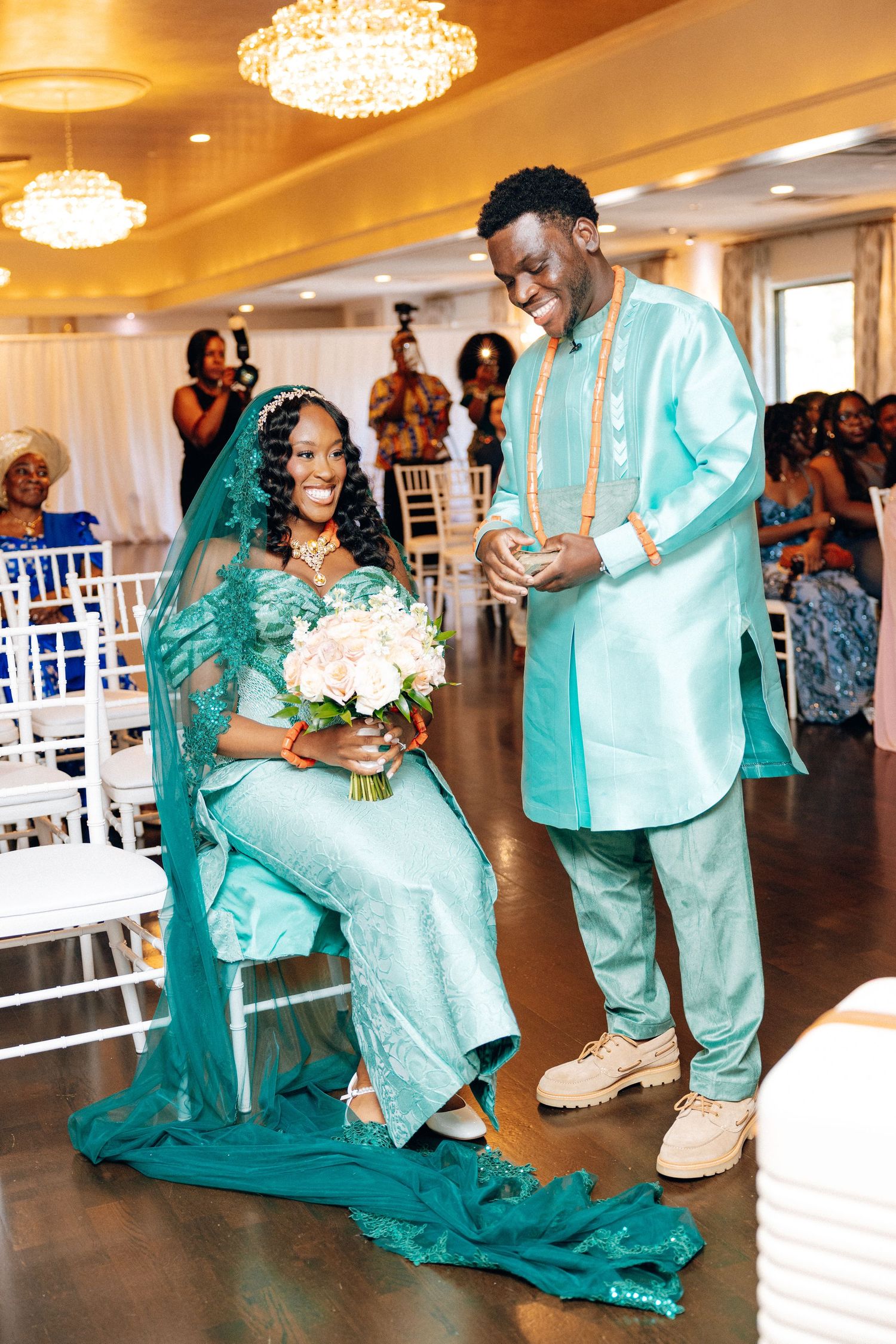 Bride and groom in matching teal African traditional wedding attire smile together at ceremony.