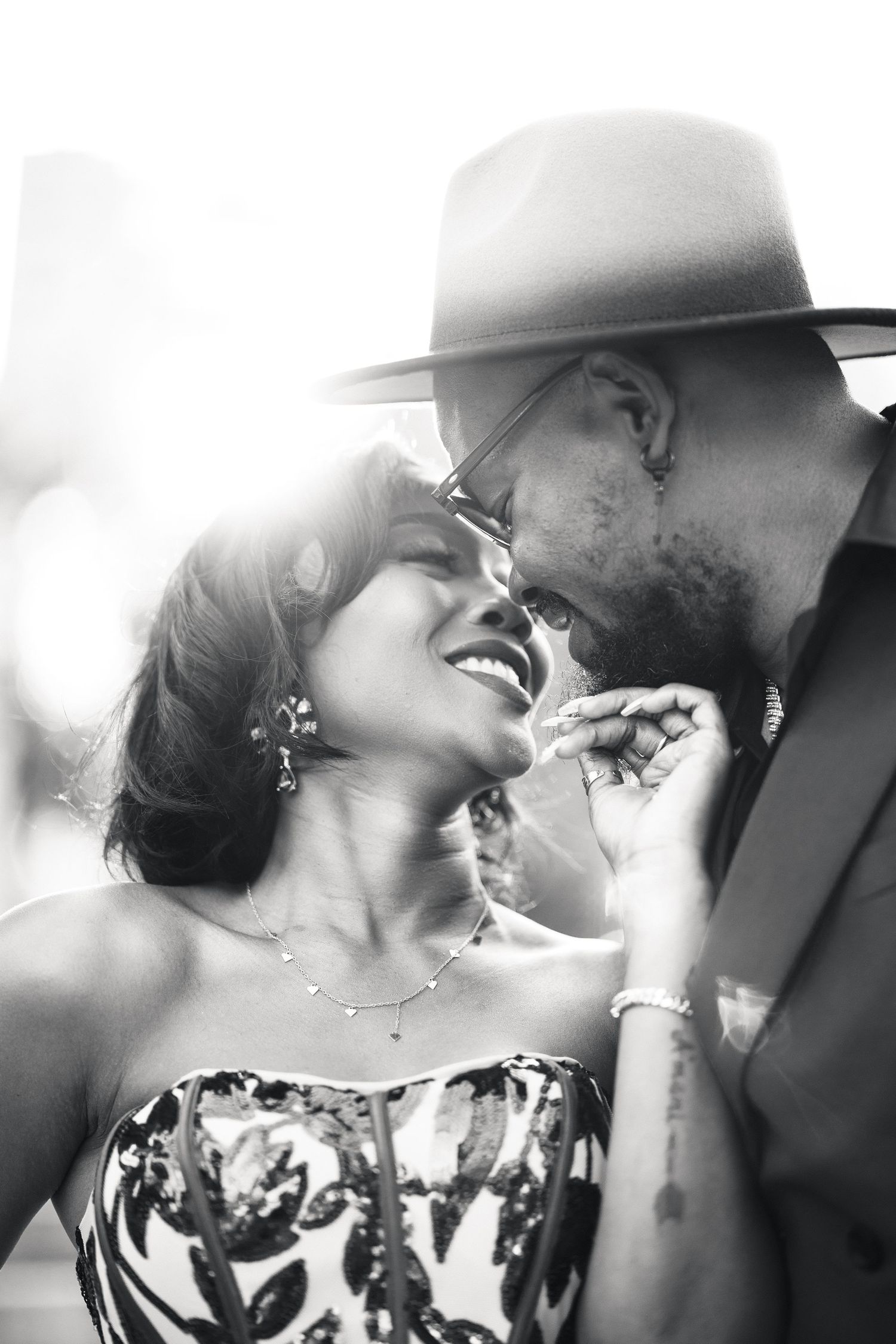 Romantic black and white close-up of a smiling couple about to kiss, man in wide-brim hat and glasses leaning toward woman.