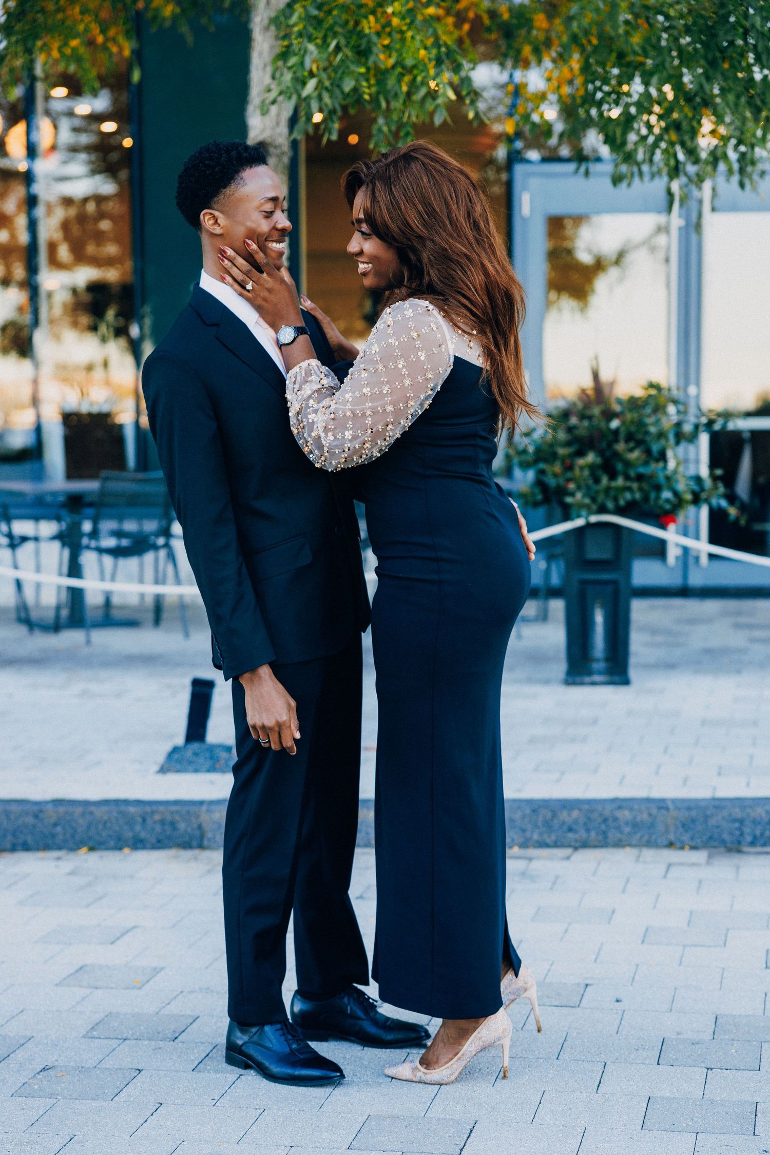 Elegant Black couple in formal attire sharing a romantic moment outdoors, woman touching mans face lovingly.
