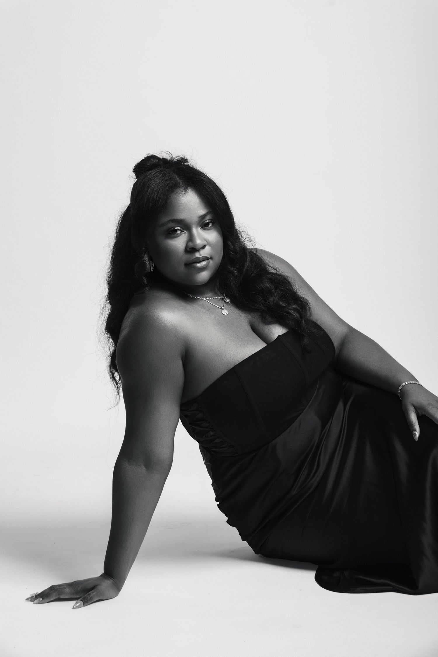 Black and white portrait of a woman in an elegant black strapless gown, posing gracefully on the floor.